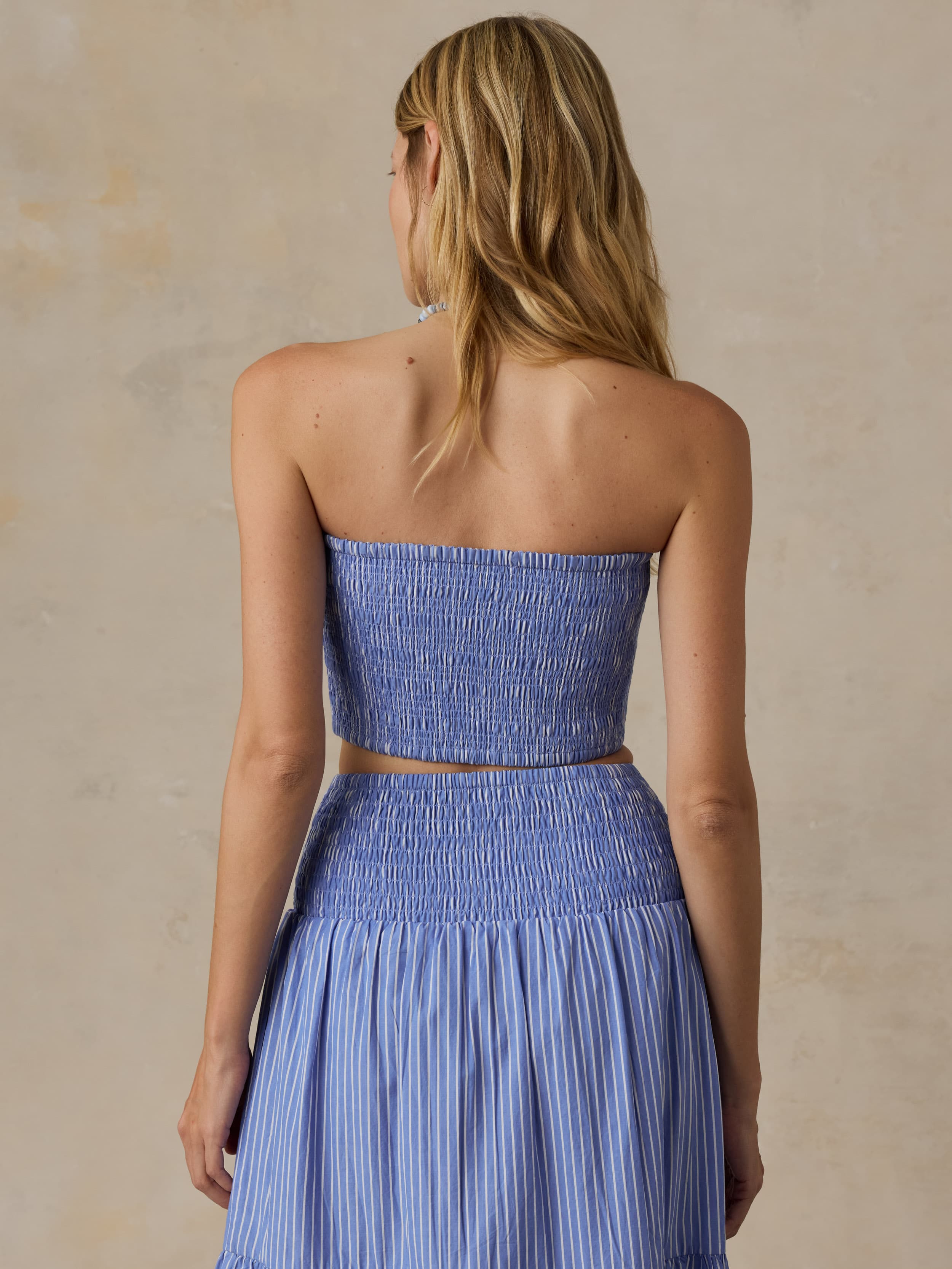 Woman wearing a blue strapless top and skirt set against a beige background