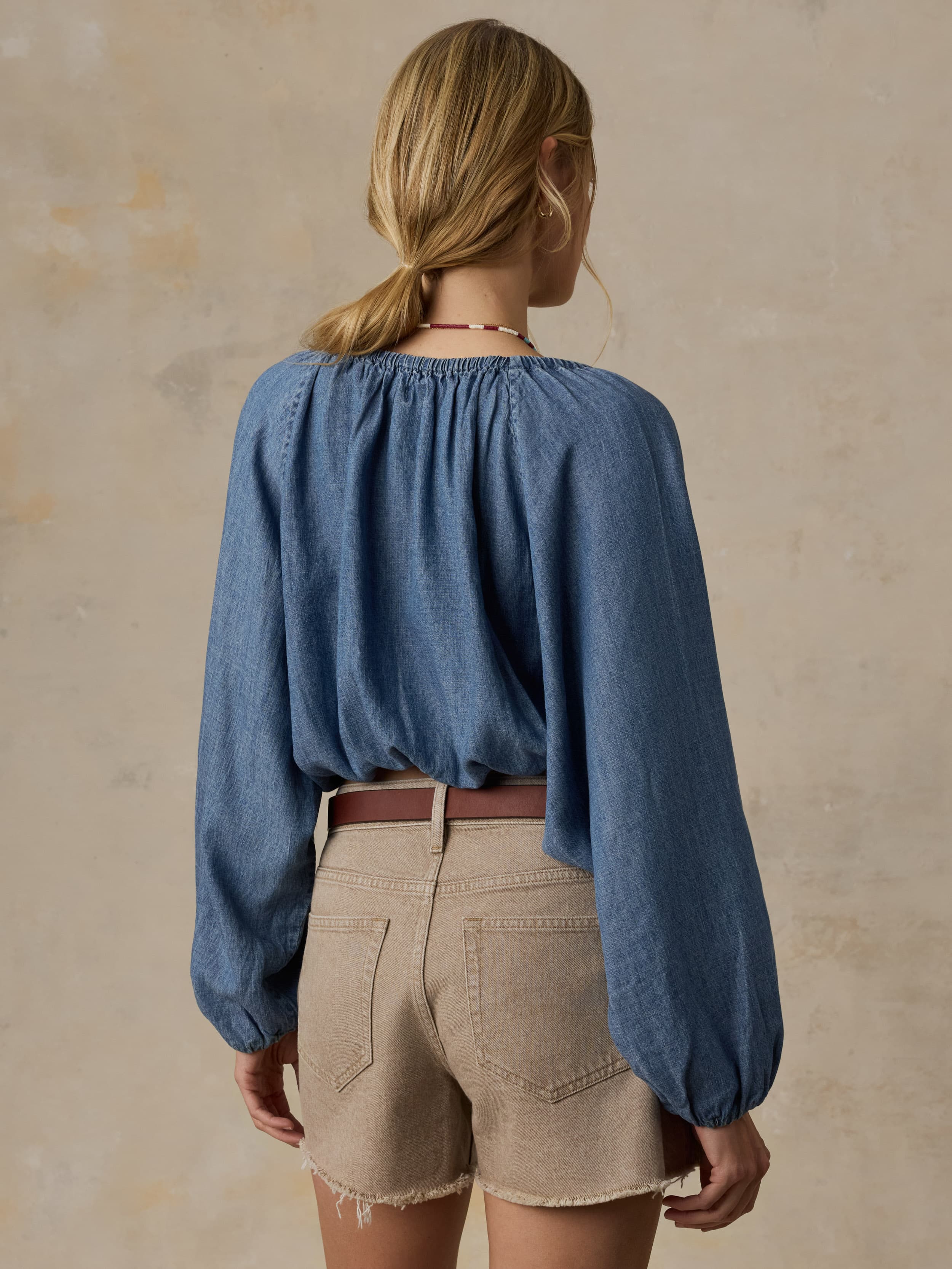 Woman wearing a blue denim top and beige shorts against a beige background