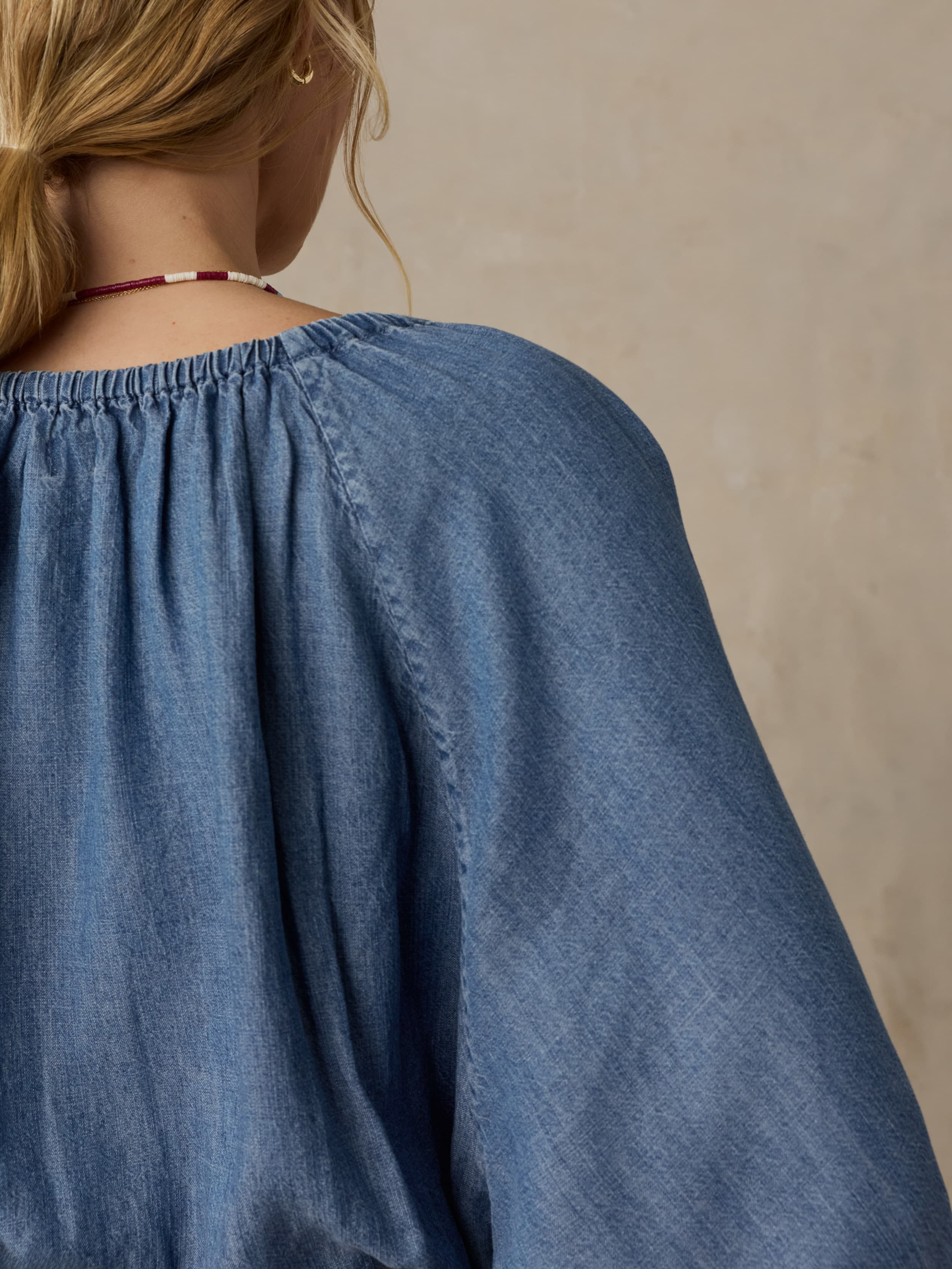 Woman wearing a blue denim top against a beige background