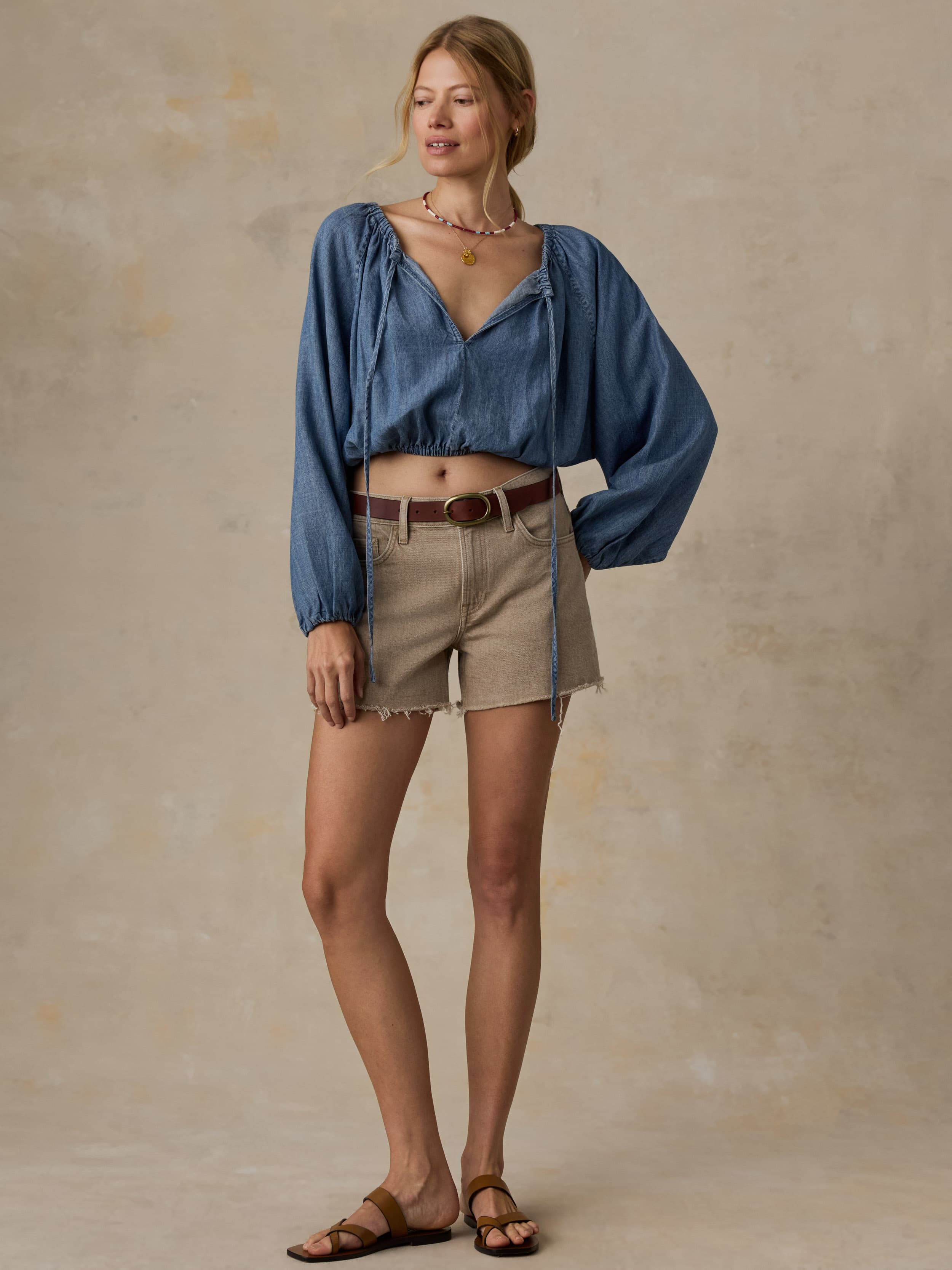 Woman wearing a blue denim top and beige shorts against a beige background