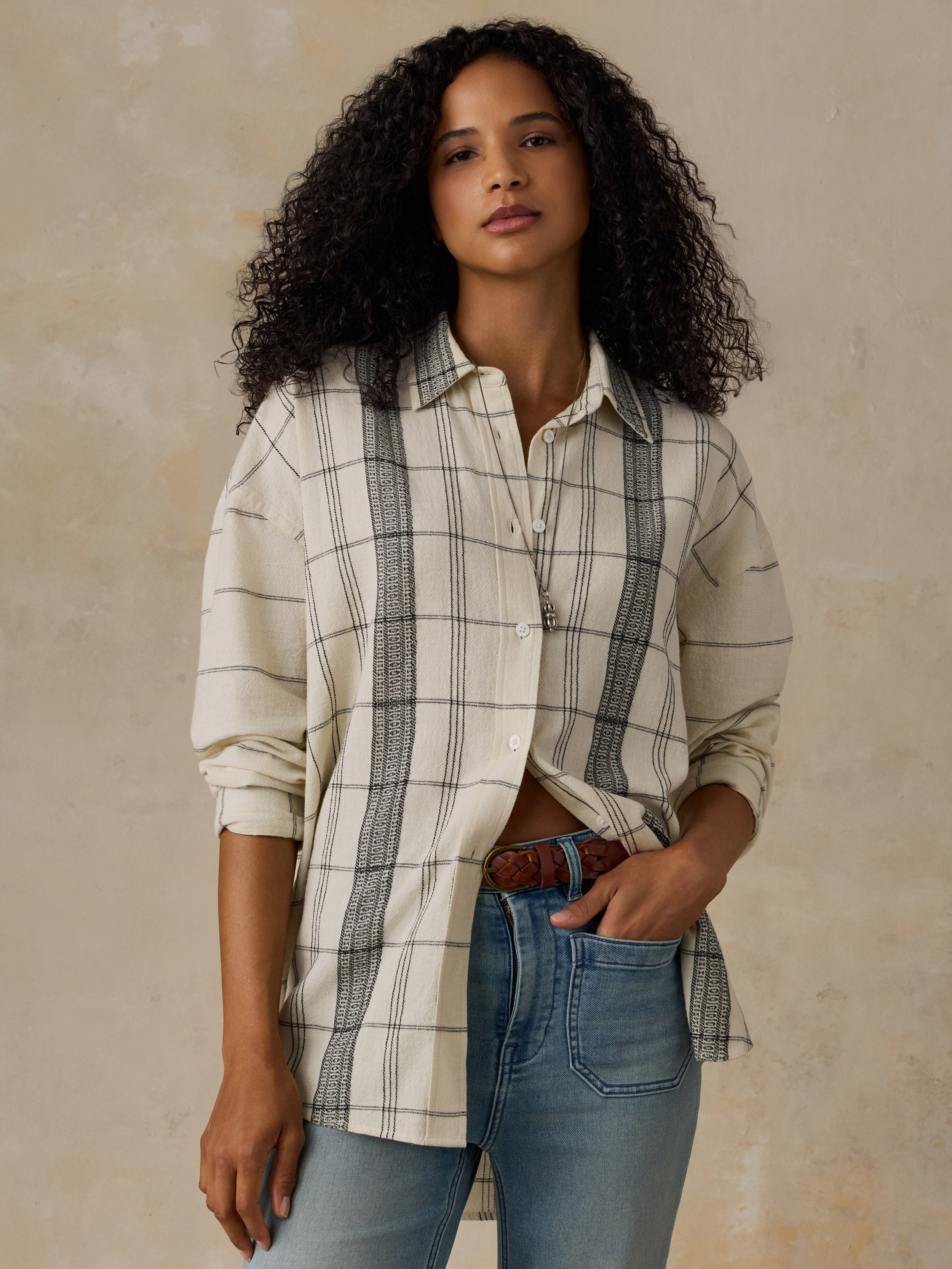 Woman wearing a white and black plaid shirt with blue jeans against a beige background