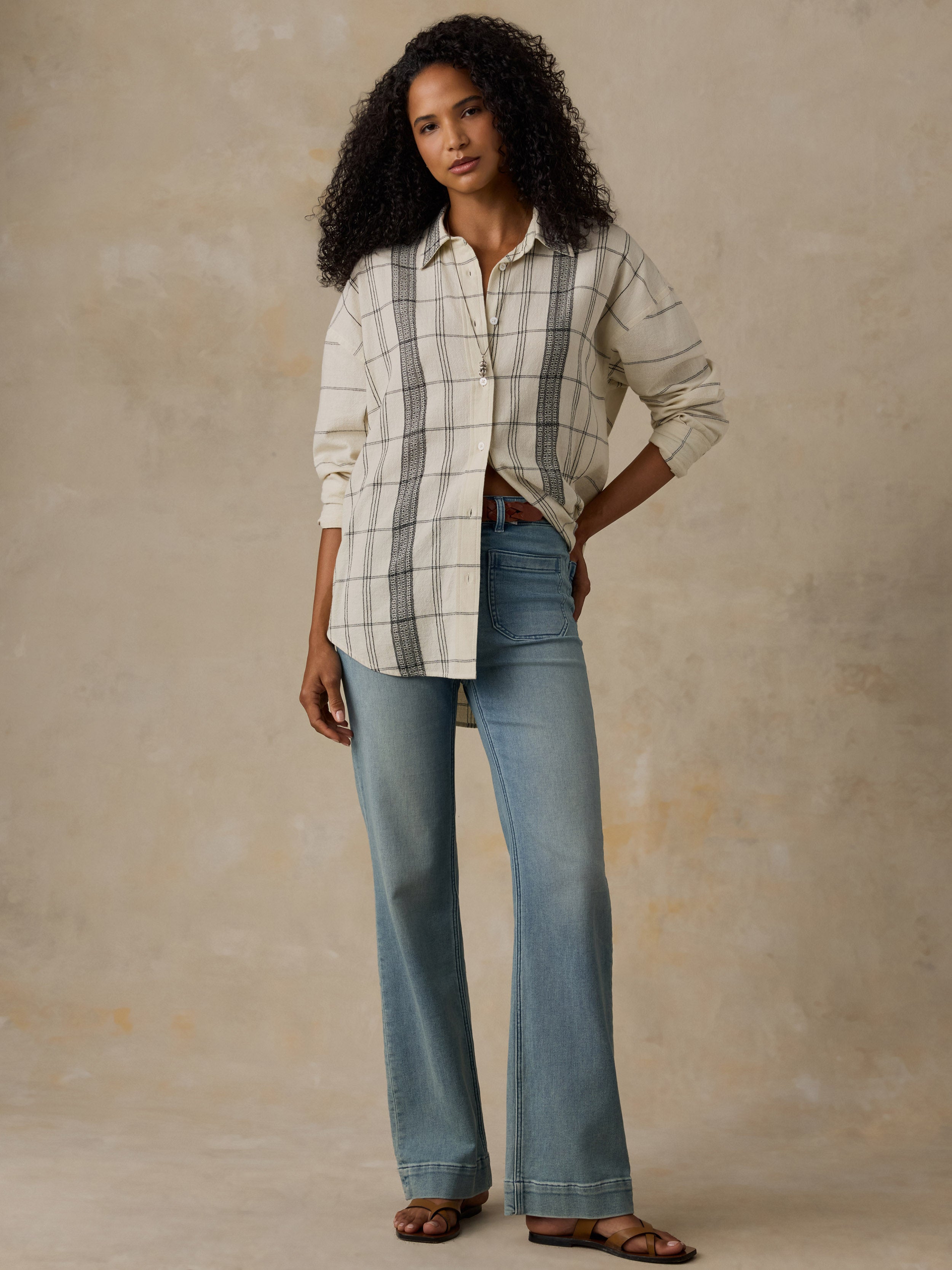 Woman wearing a white and black plaid shirt with blue jeans against a beige background
