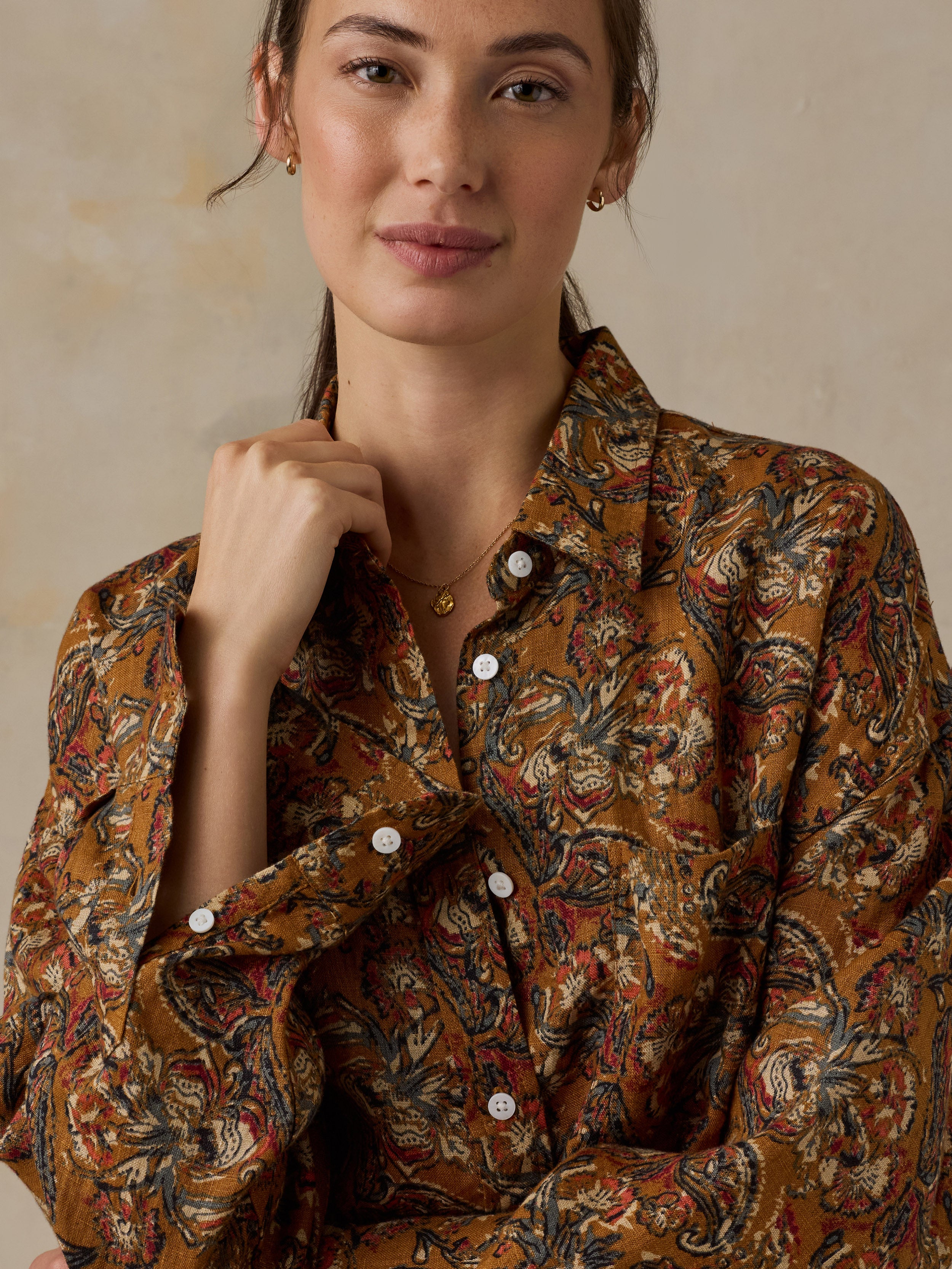 Woman wearing an orange floral printed button down shirt against a beige background