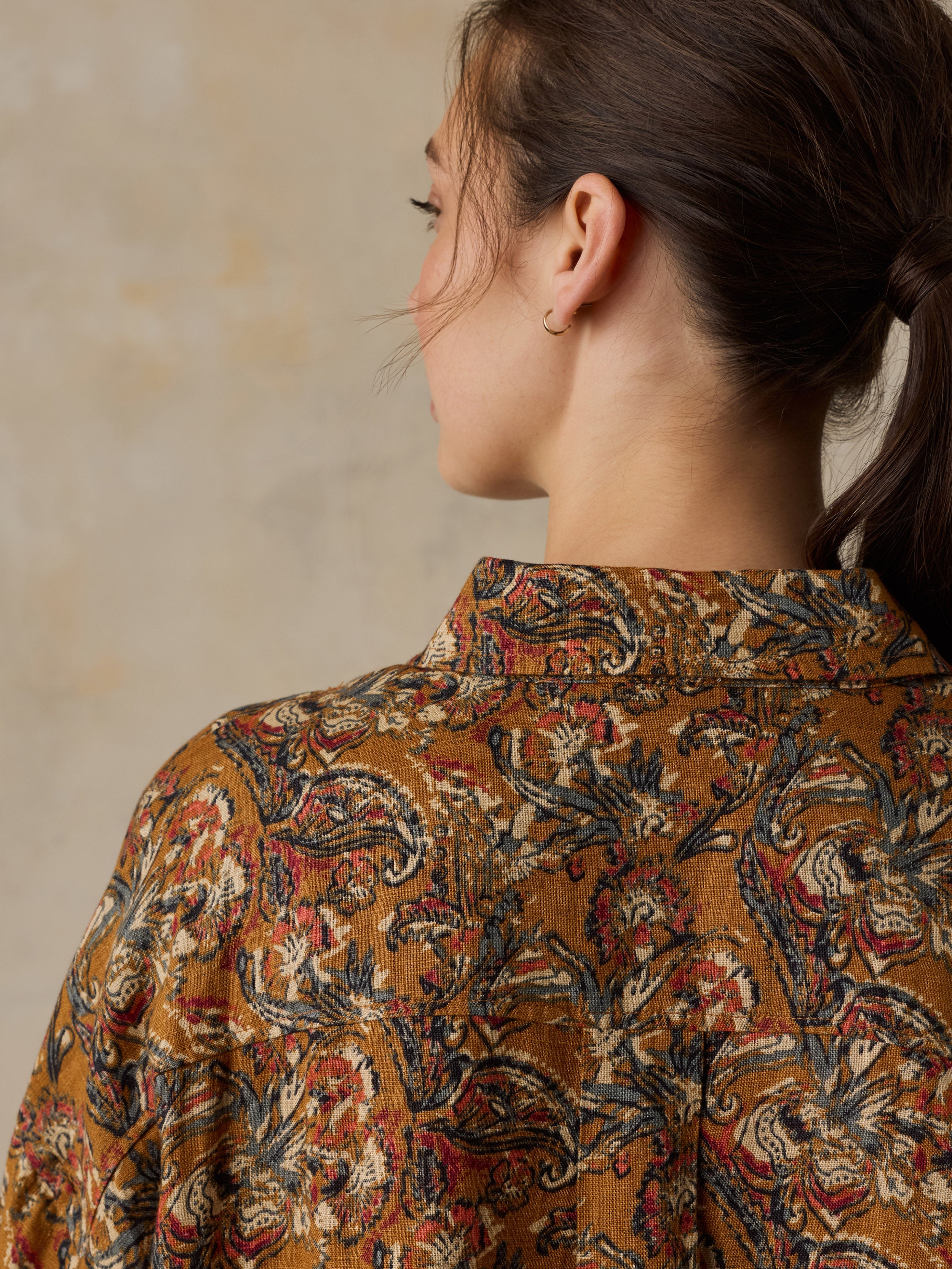 Woman wearing an orange floral printed button down shirt against a beige background