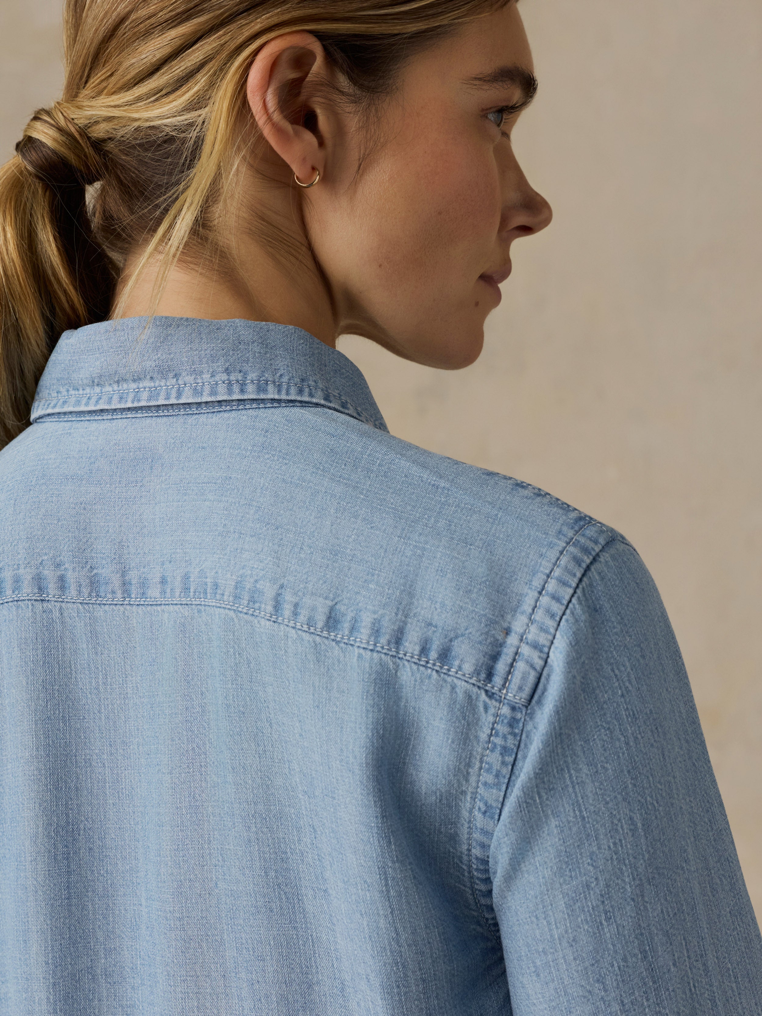 Woman wearing a chambray button down shirt against a beige background