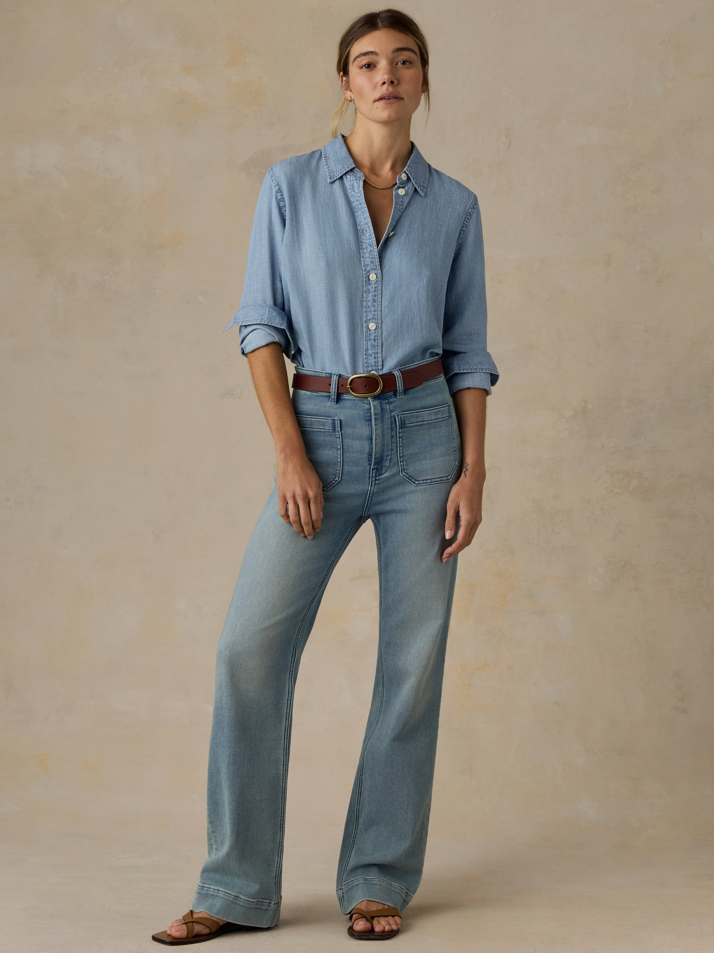 Woman wearing a chambray button down shirt with blue jeans against a beige background