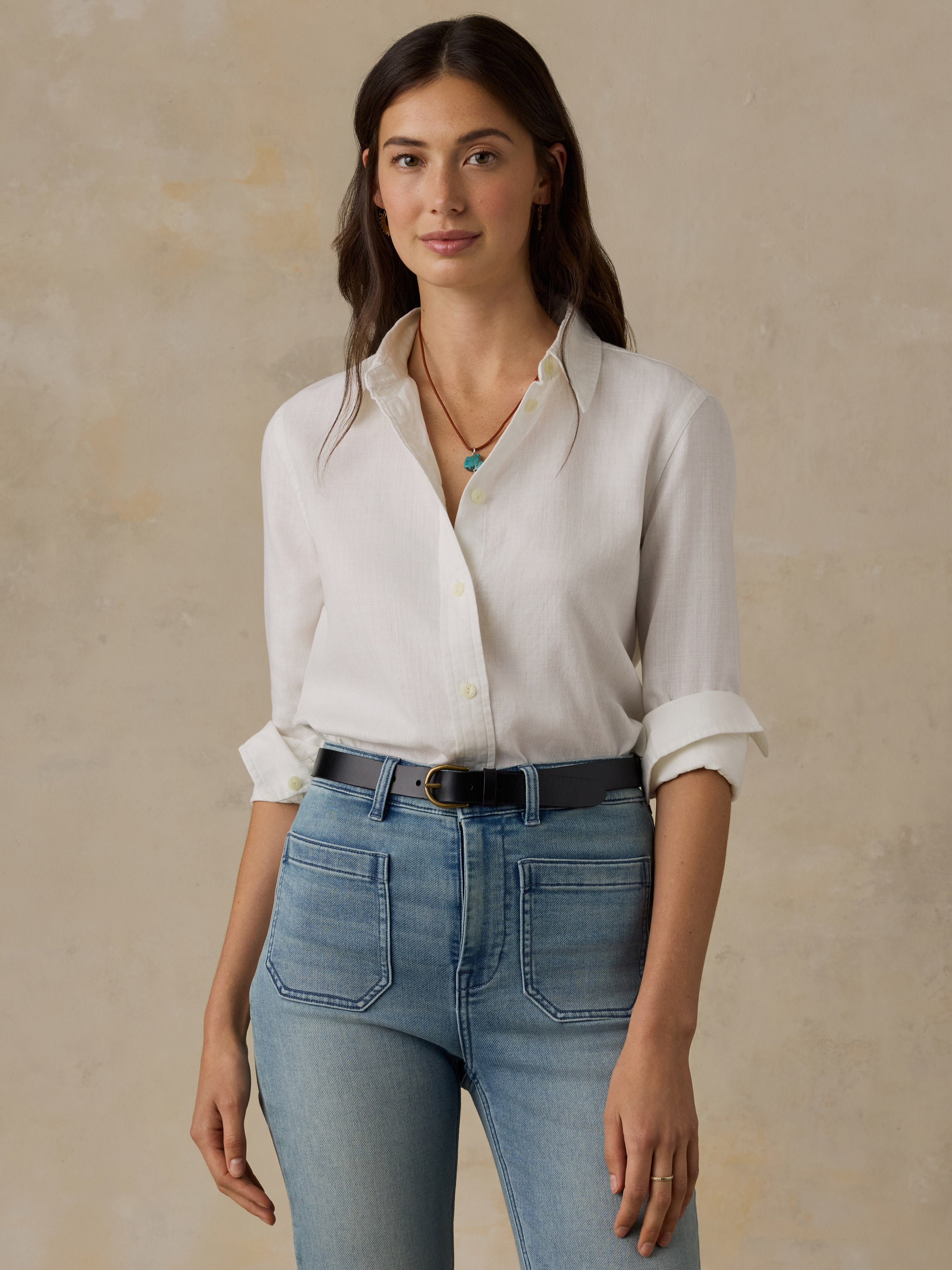 Woman wearing a white chambray button down shirt and blue jeans against a beige background