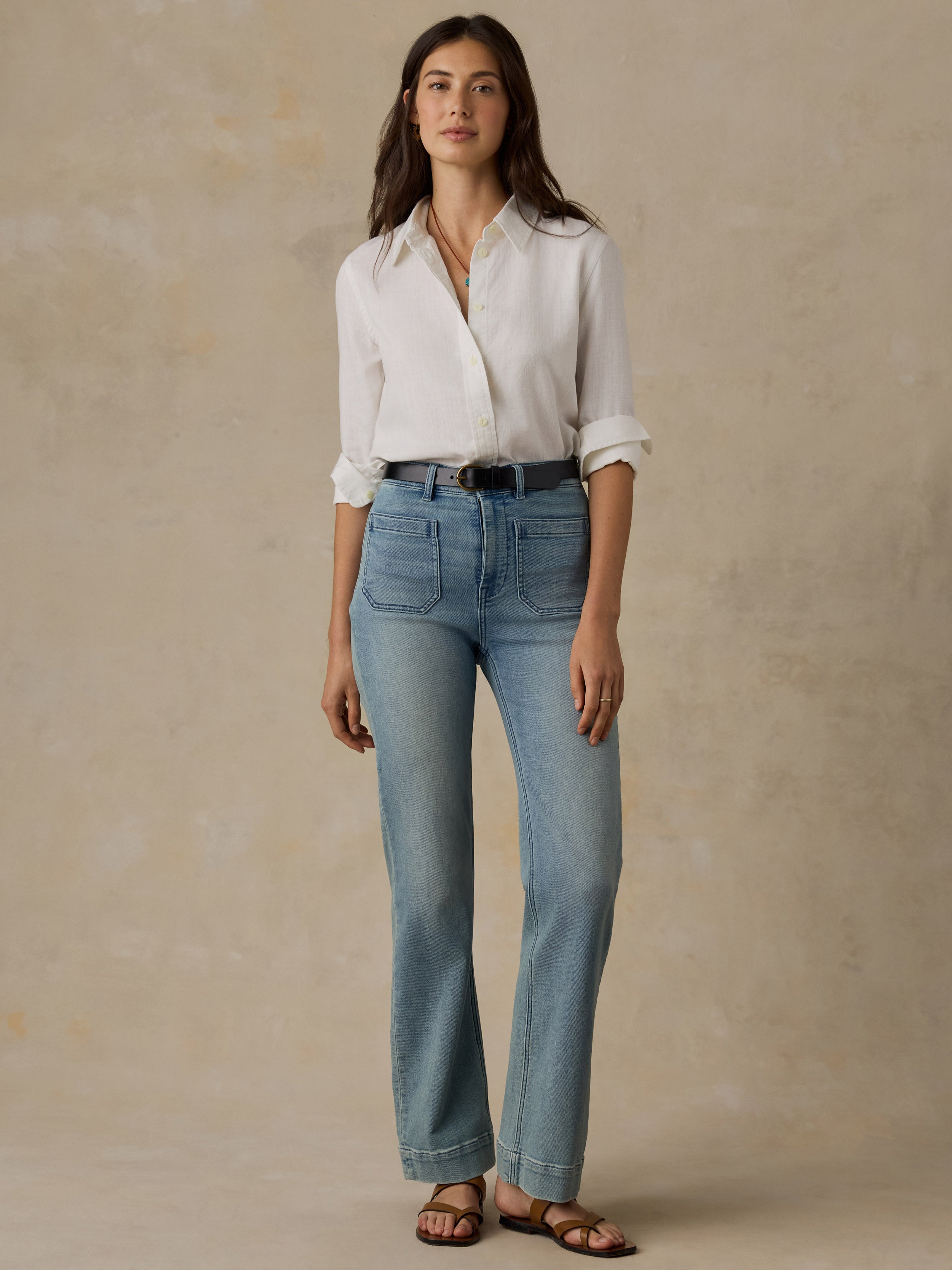 Woman wearing a white chambray button down shirt and blue jeans against a beige background