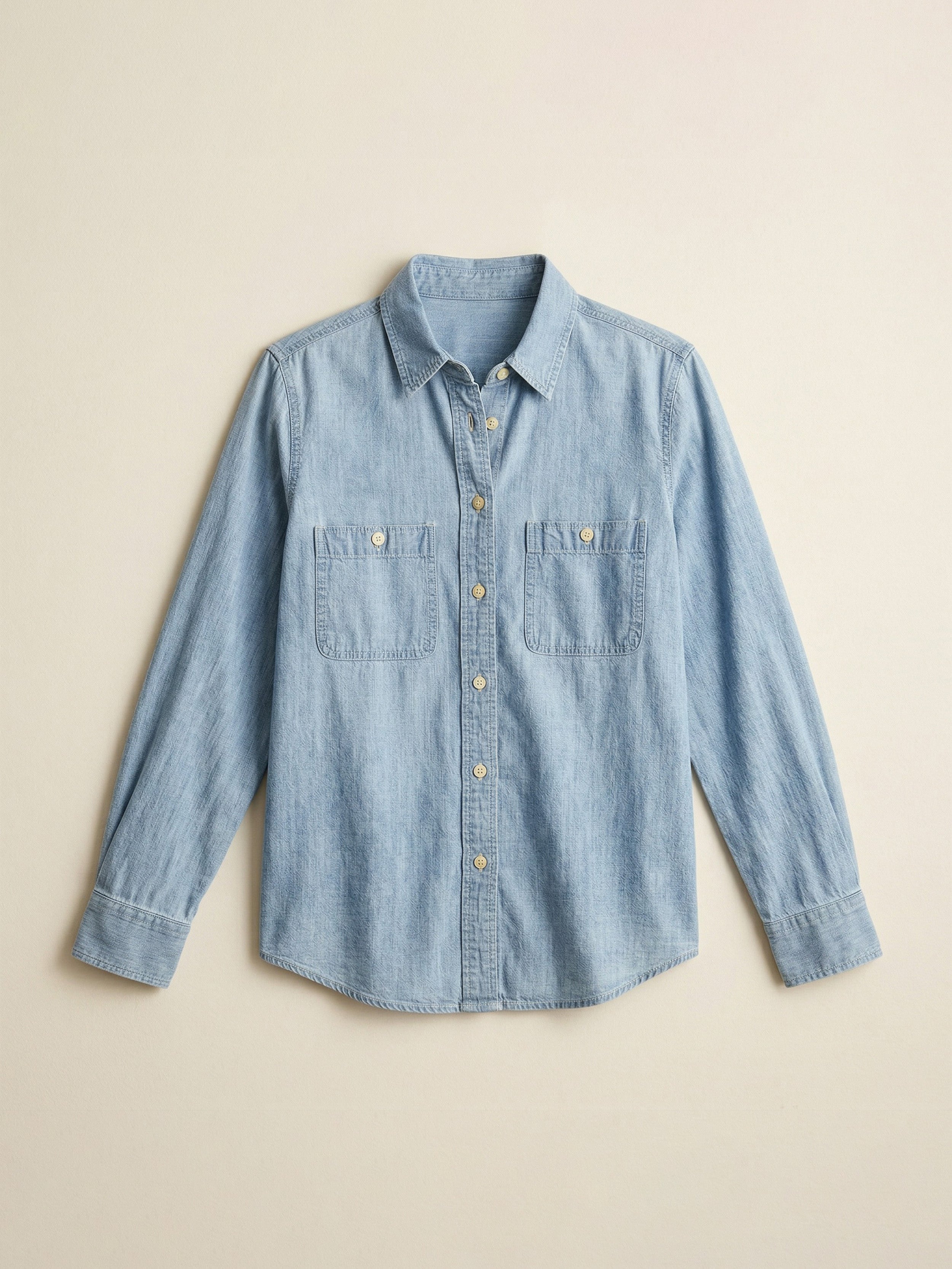 Flat image of a light blue chambray shirt against a beige background