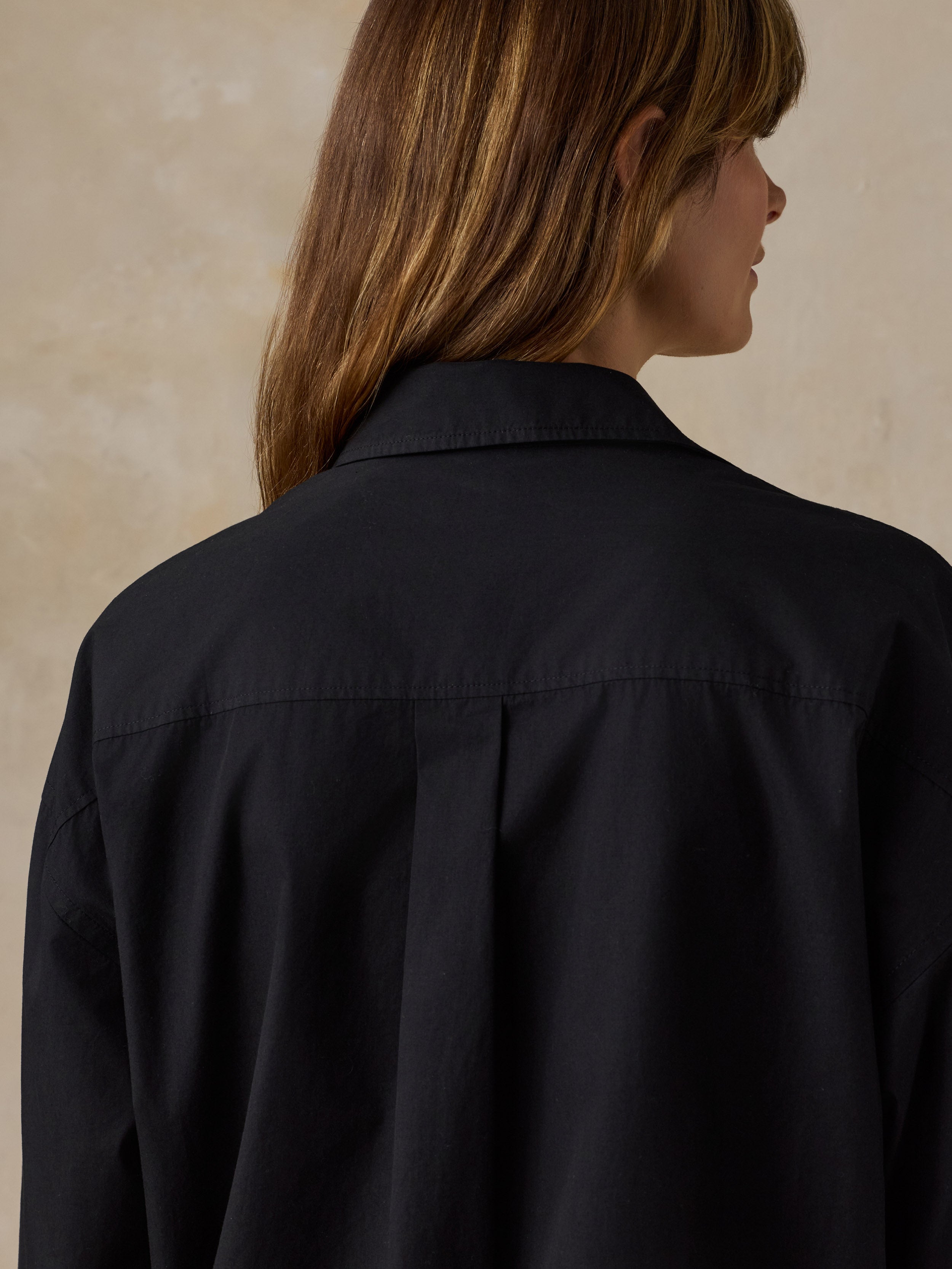 Woman wearing a black button down shirt against a beige background