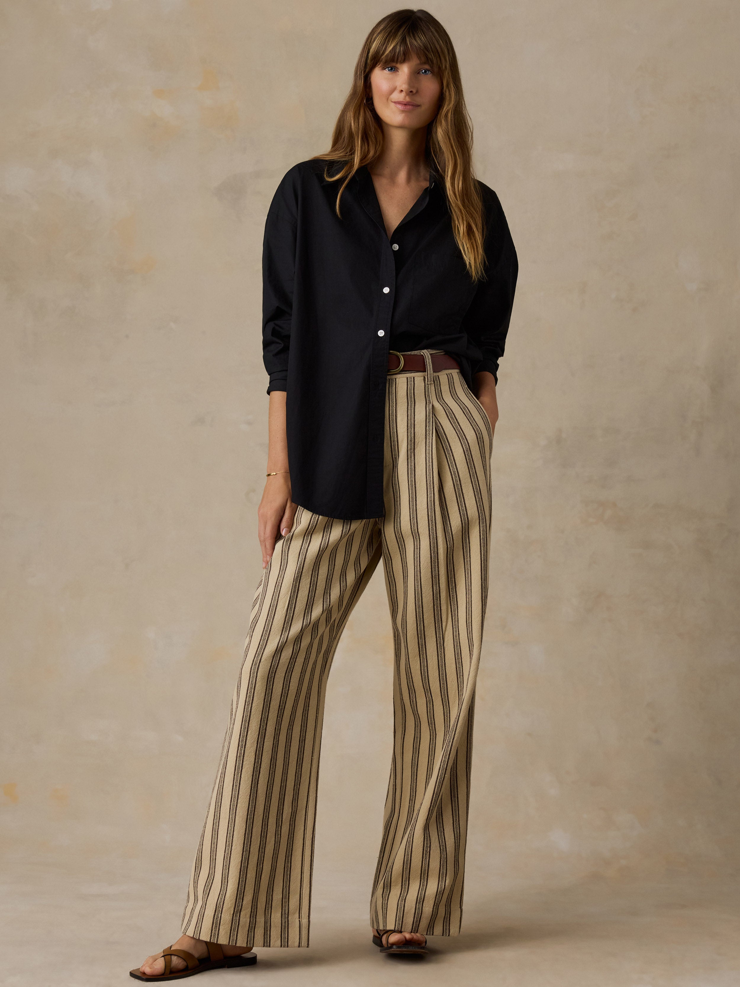 Woman wearing a black button down shirt and beige striped pants against a beige background