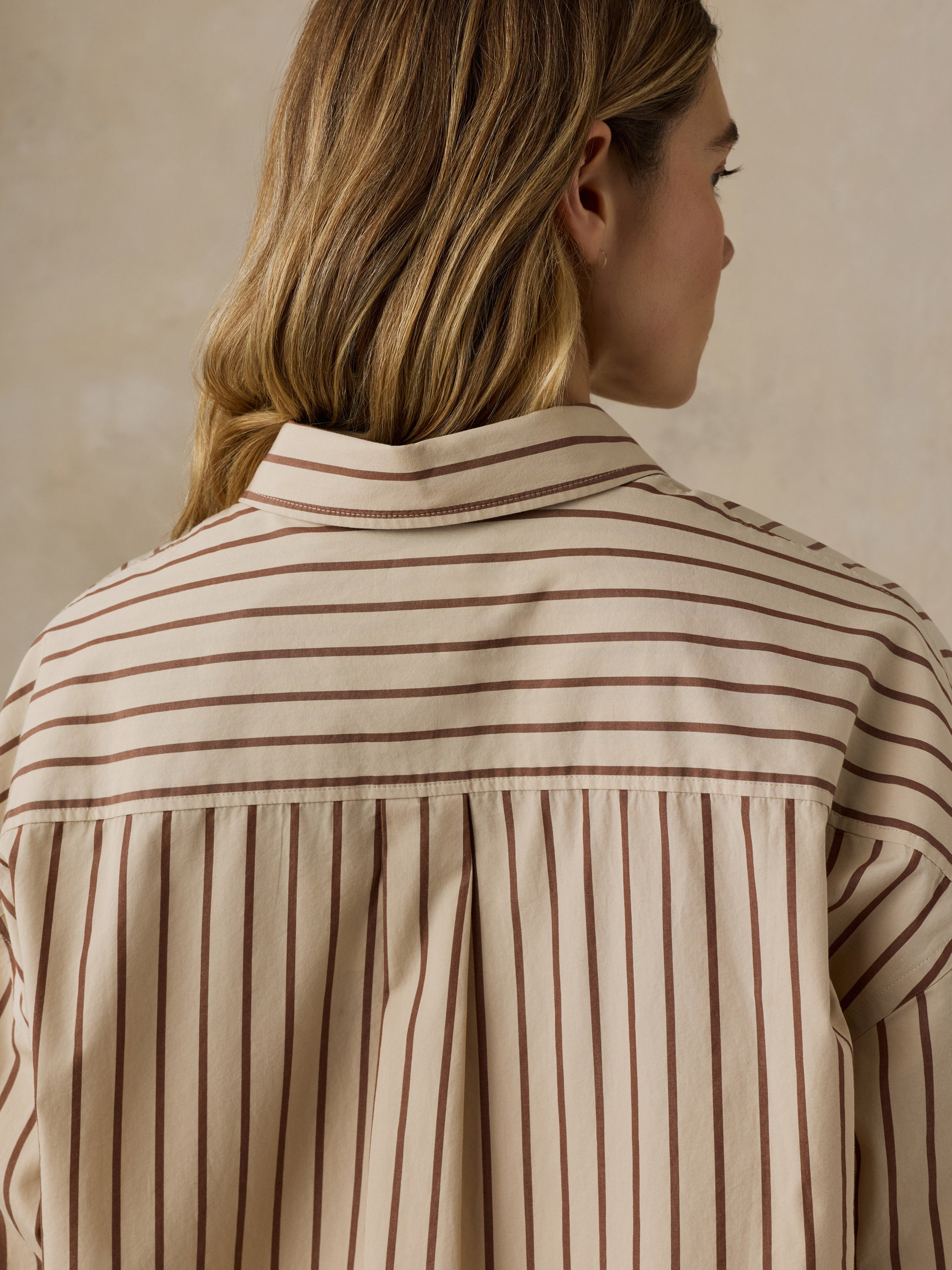 Woman wearing a beige and brown striped button down shirt against a beige background