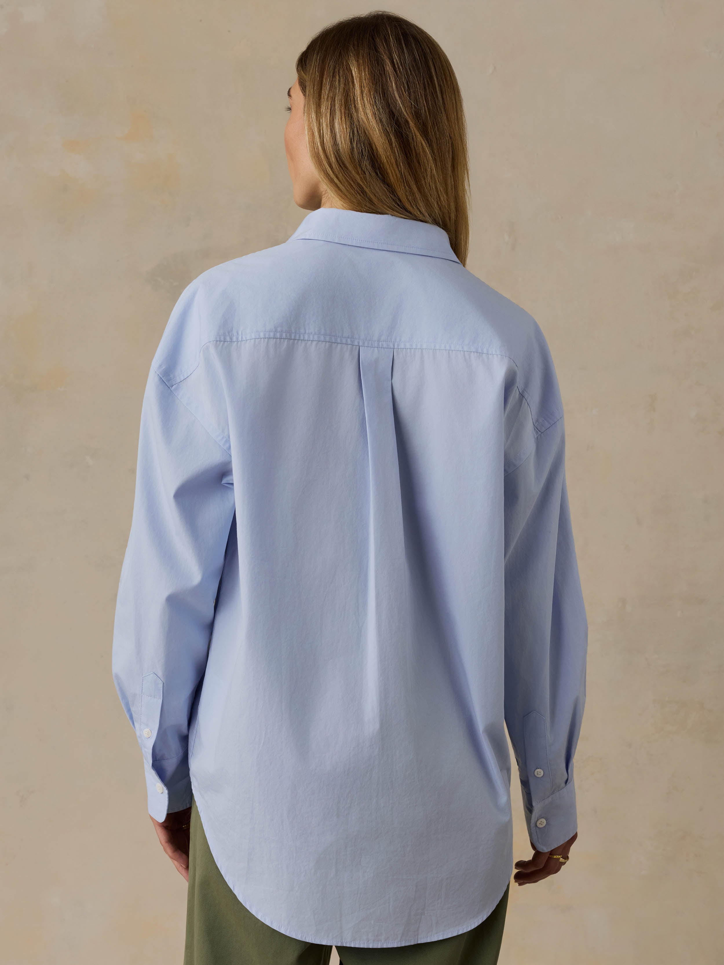 Woman wearing a light blue shirt and green pants against a beige background