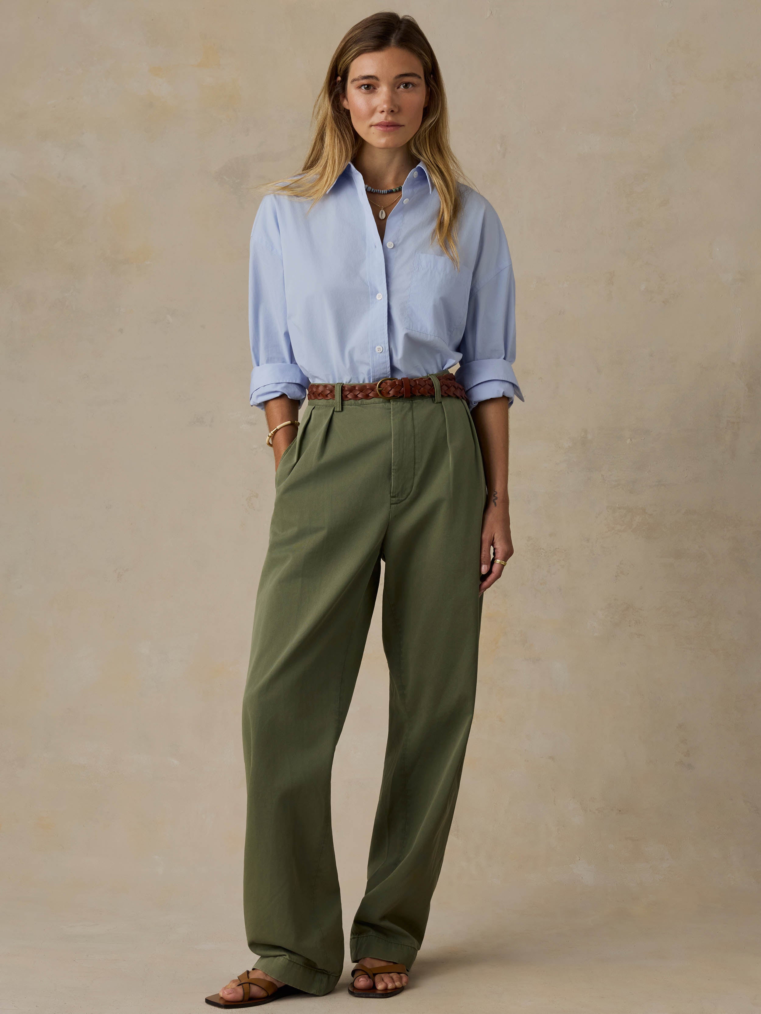 Woman wearing a light blue shirt and green pants against a beige background