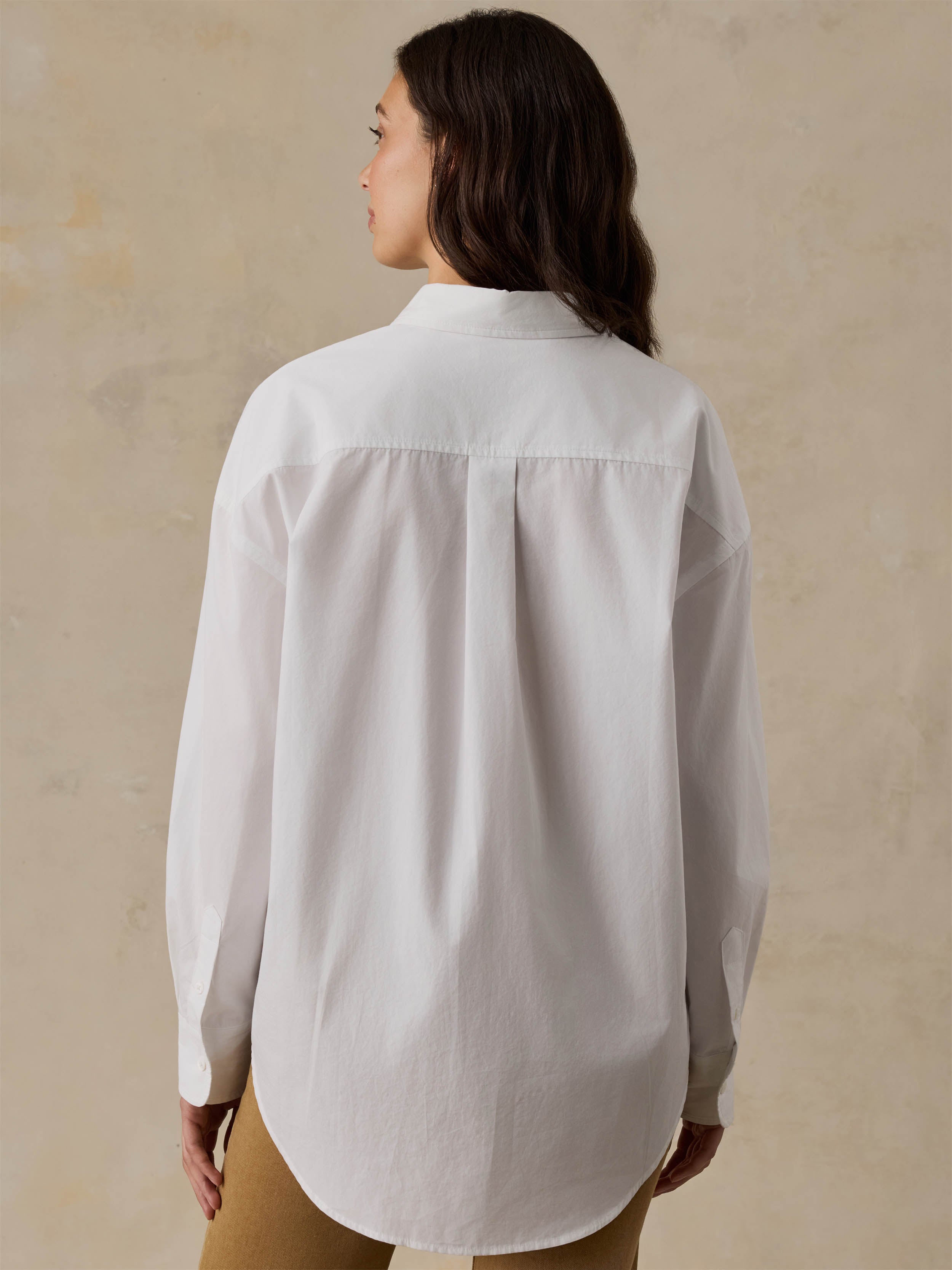 Woman wearing a white shirt and brown pants against a beige background