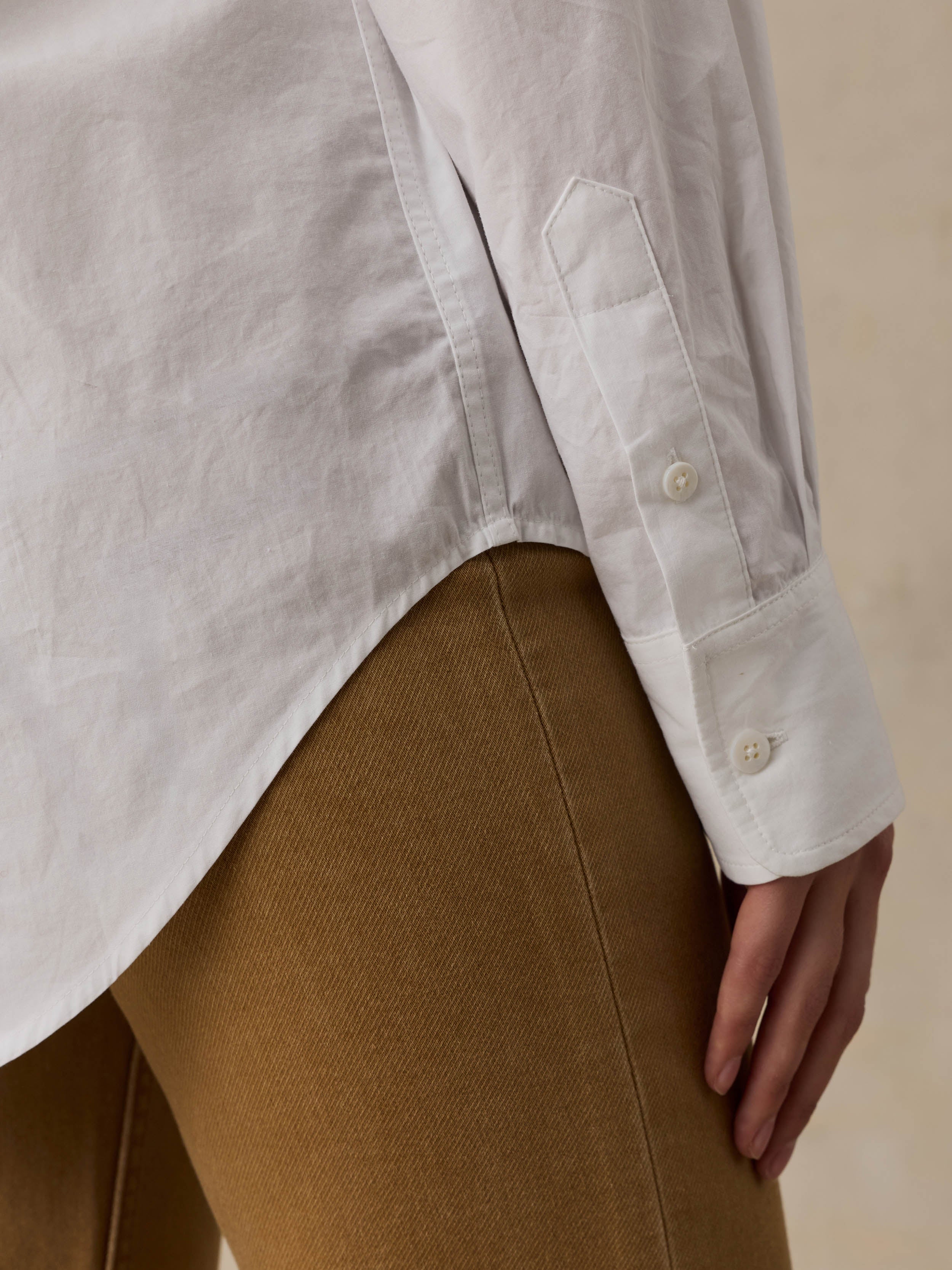 Woman wearing a white shirt and brown pants against a beige background