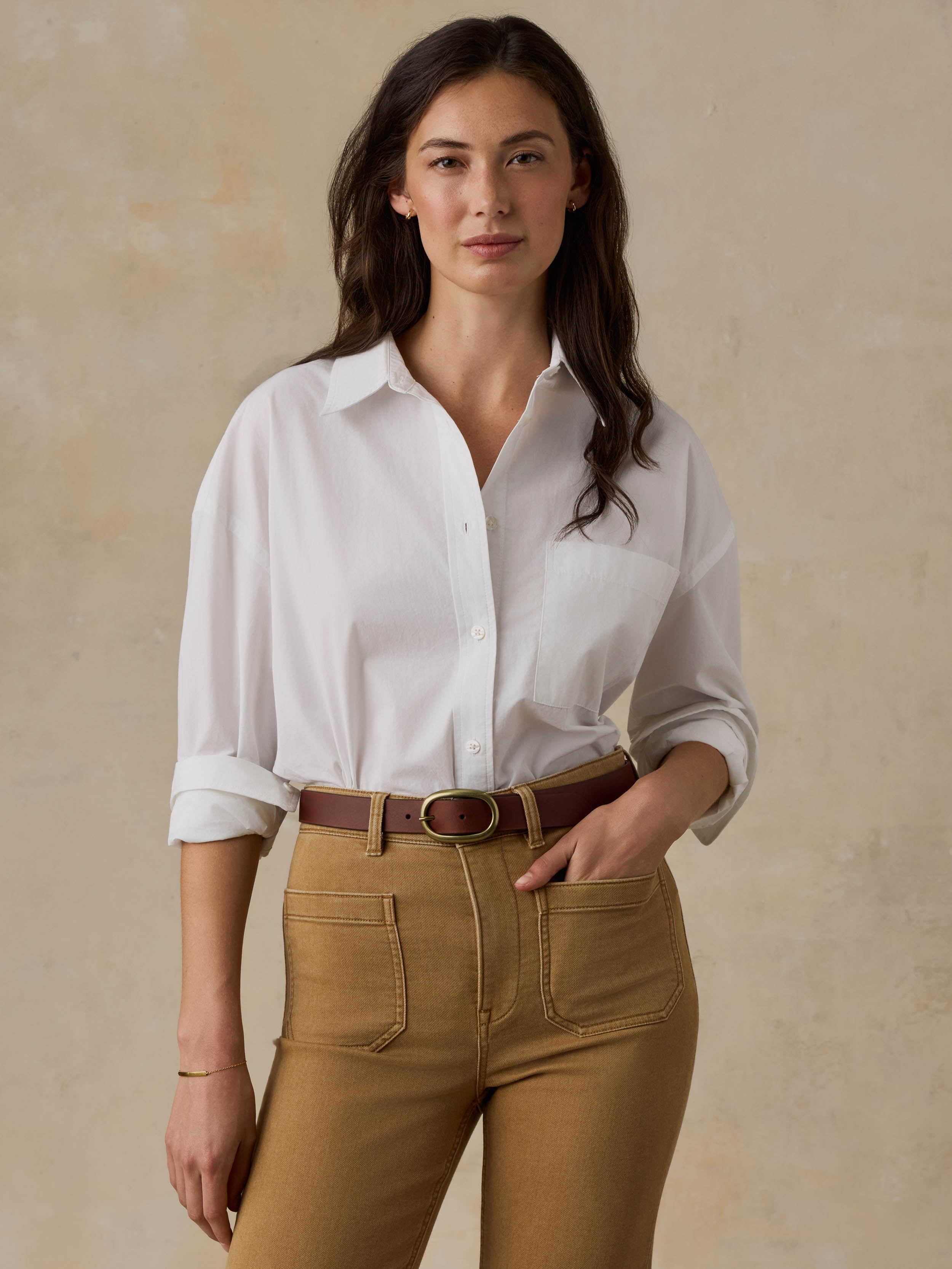 Woman wearing a white shirt and brown pants against a beige background