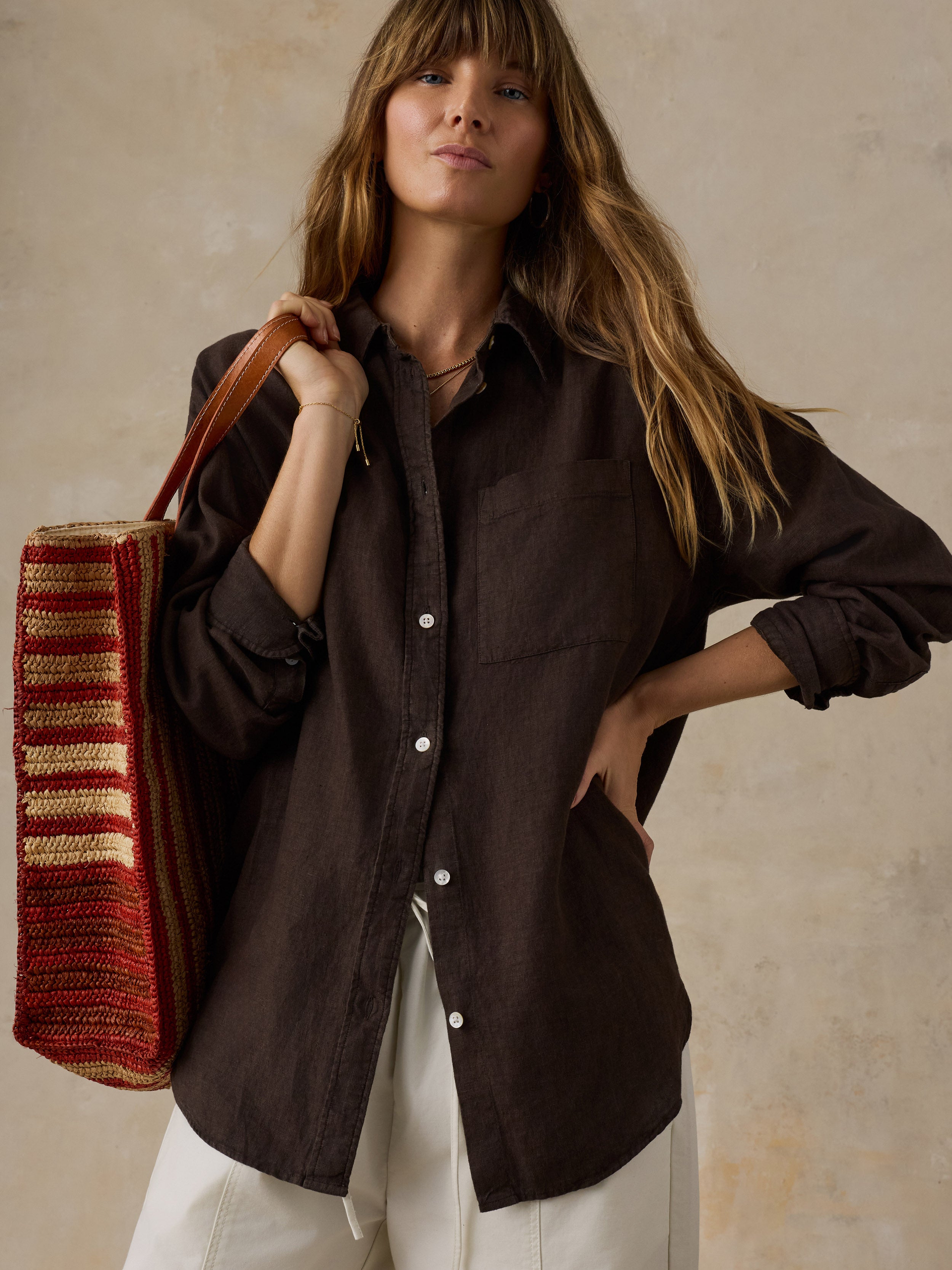 Woman wearing a brown linen shirt with light colored pants against a beige background