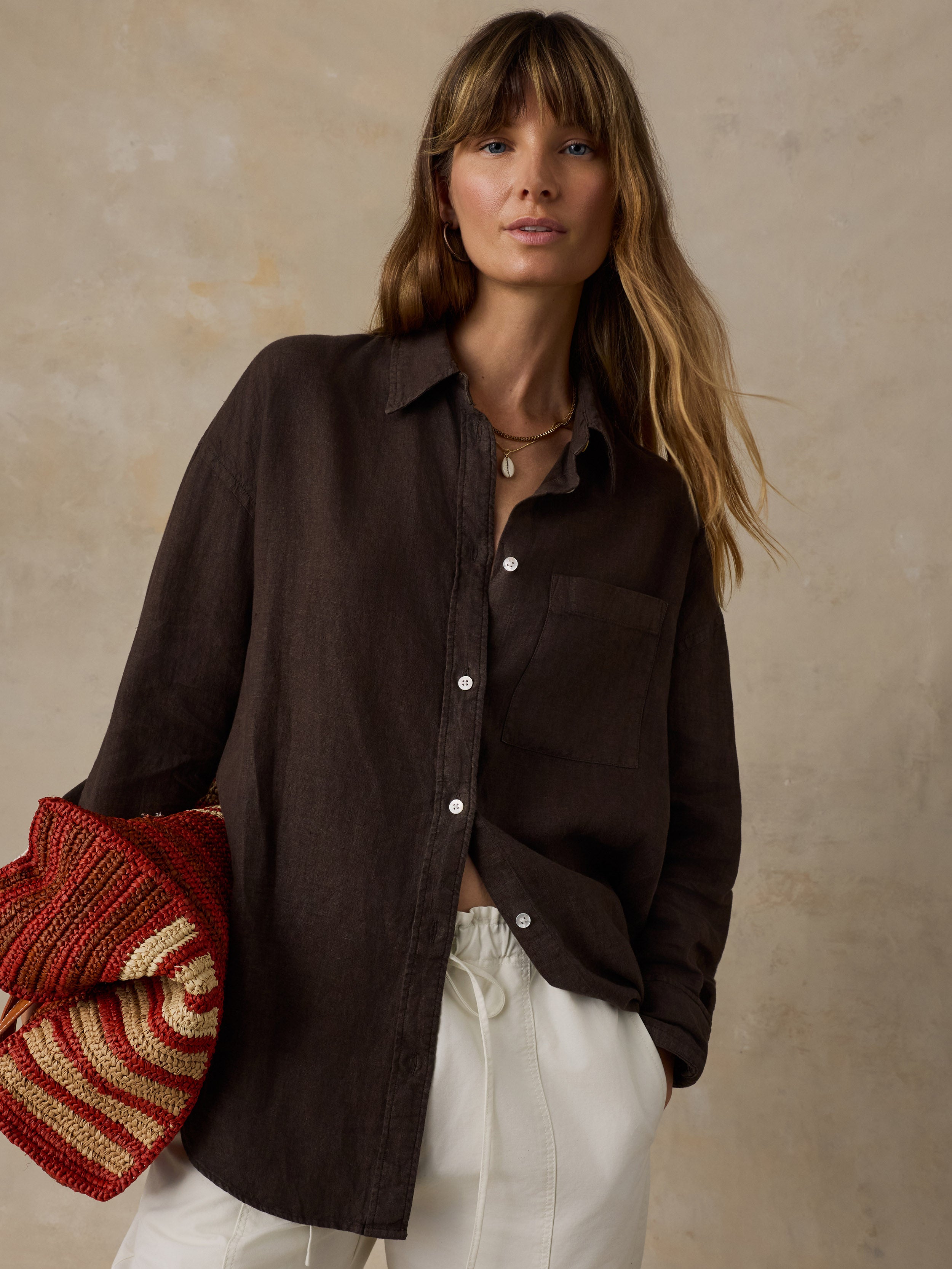 Woman wearing a brown linen shirt with light colored pants against a beige background