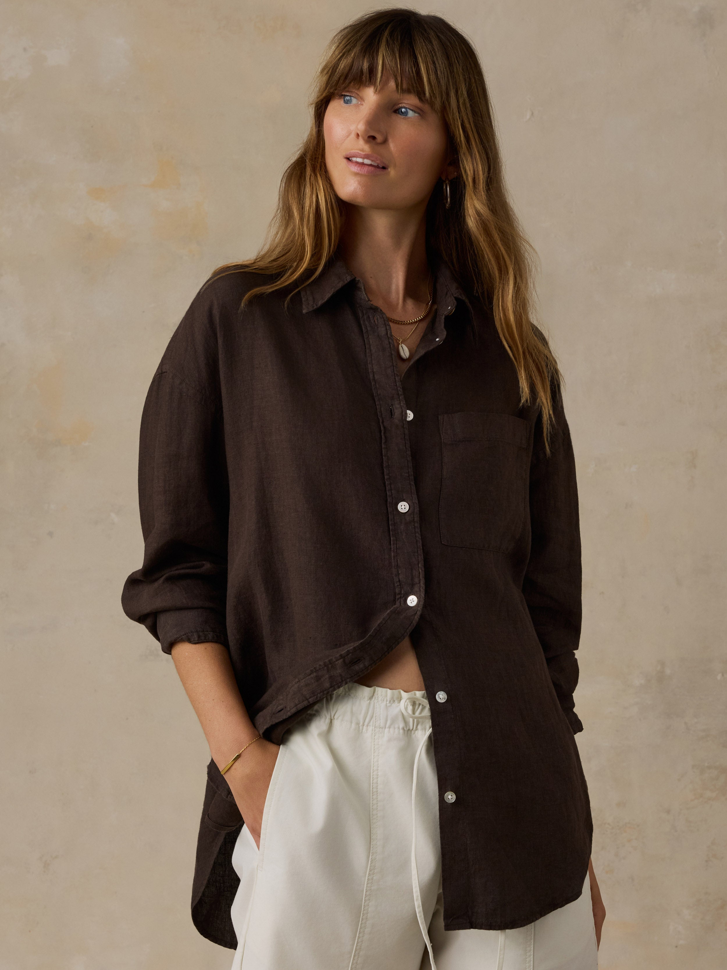 Woman wearing a brown linen shirt with light colored pants against a beige background