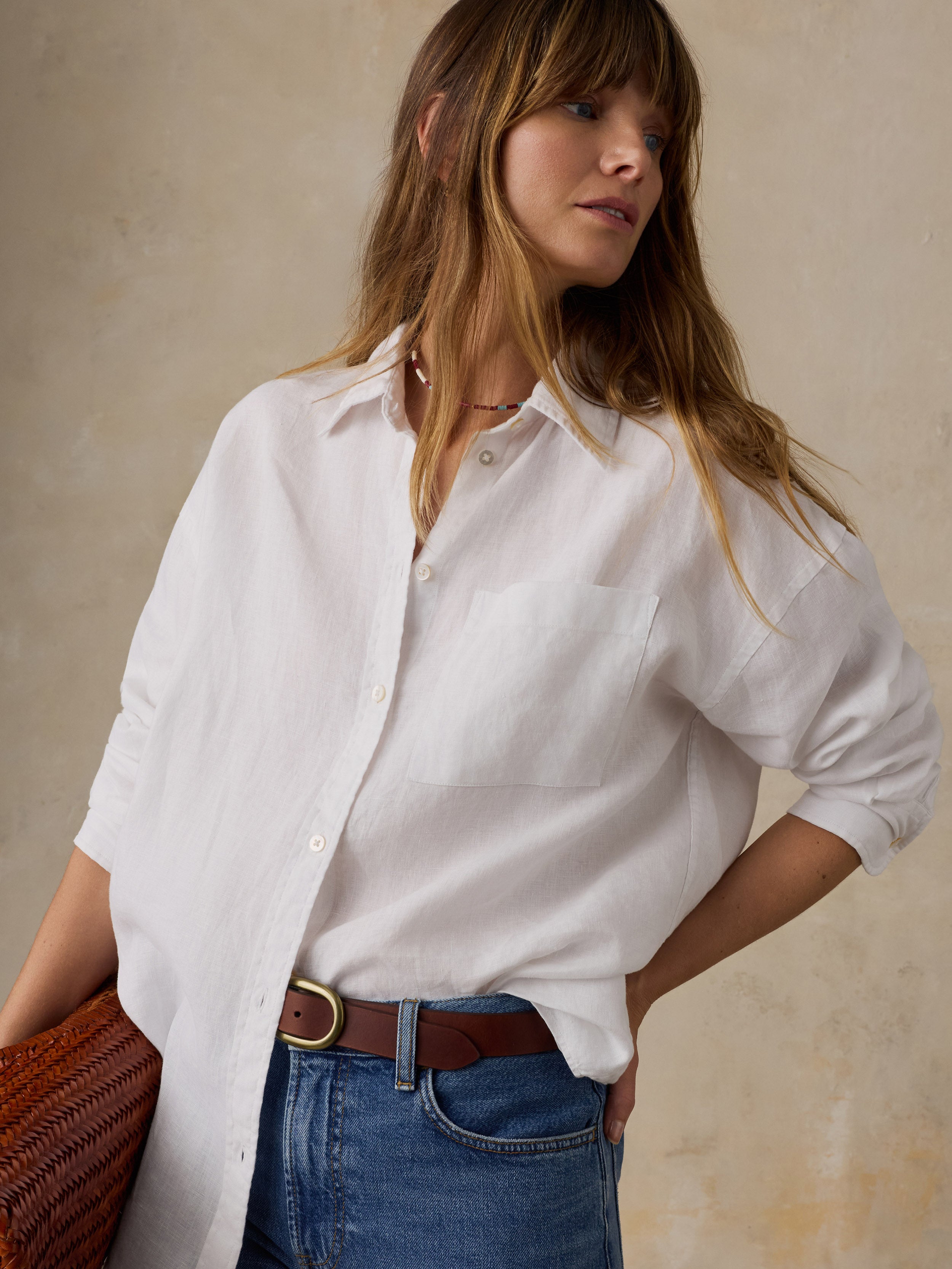 Woman wearing a white linen button down shirt with blue jeans against a beige background