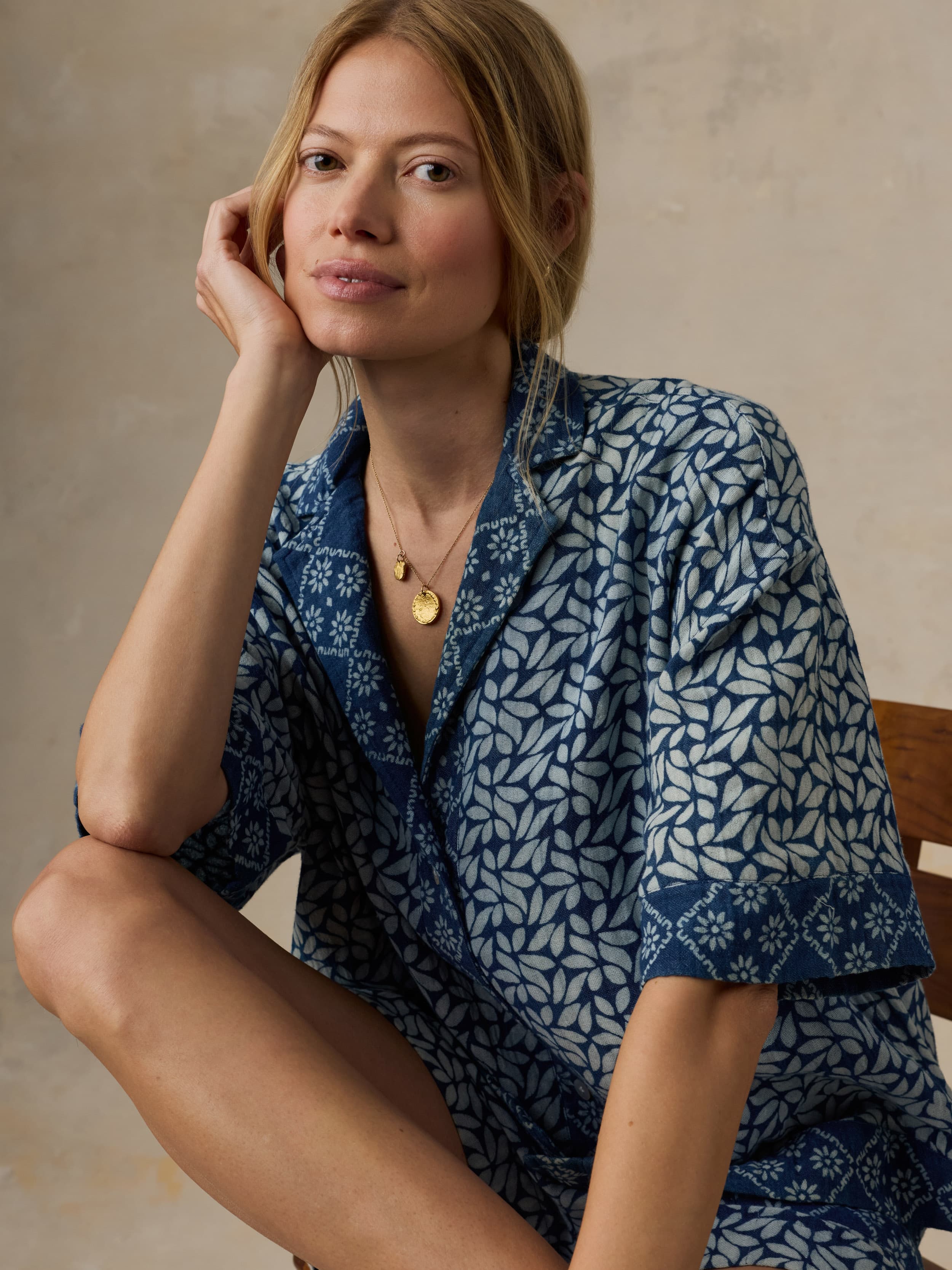 Woman wearing a blue patterned outfit sitting against a beige background