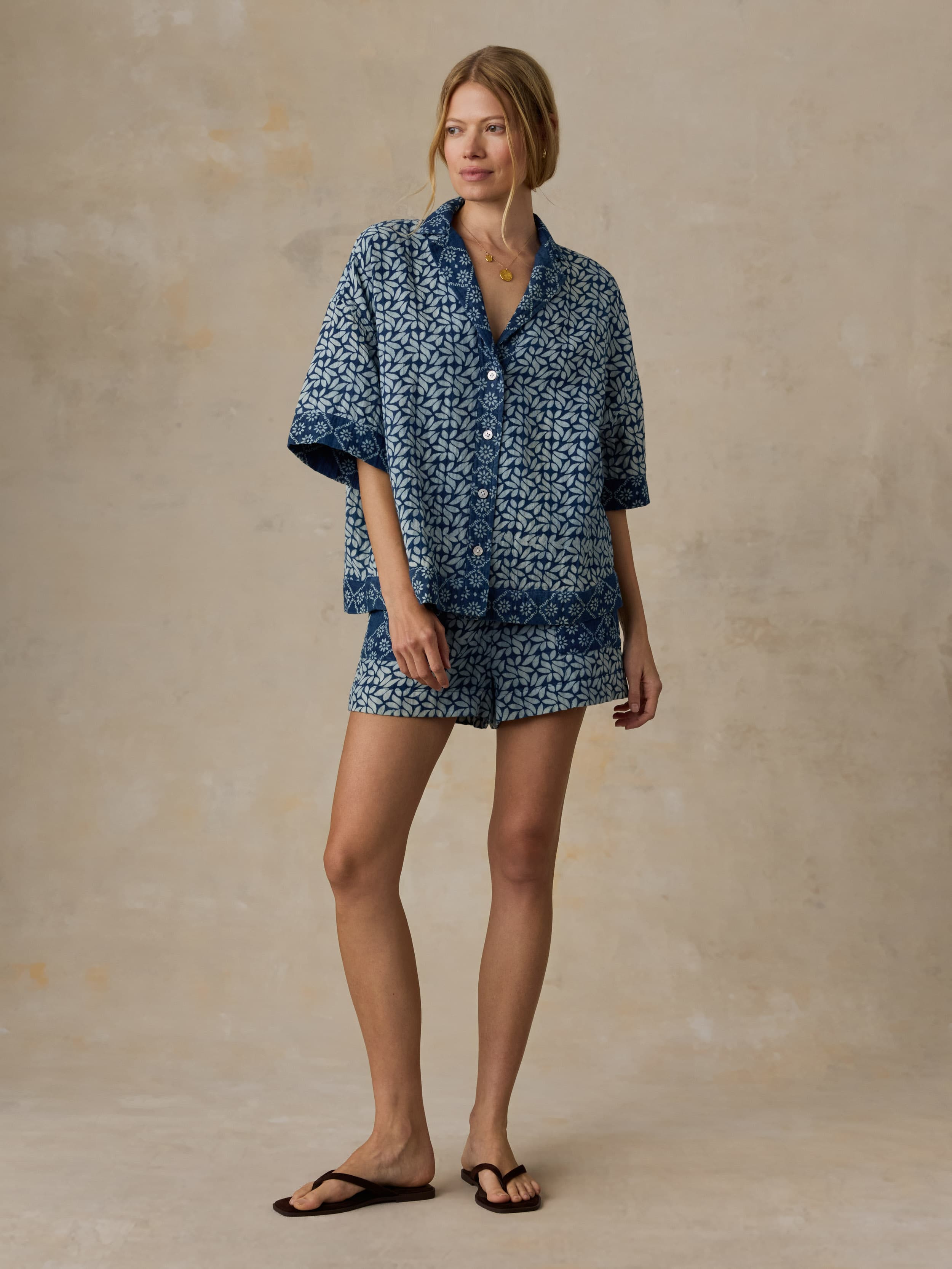 Woman wearing a blue patterned shirt and matching shorts against a beige background