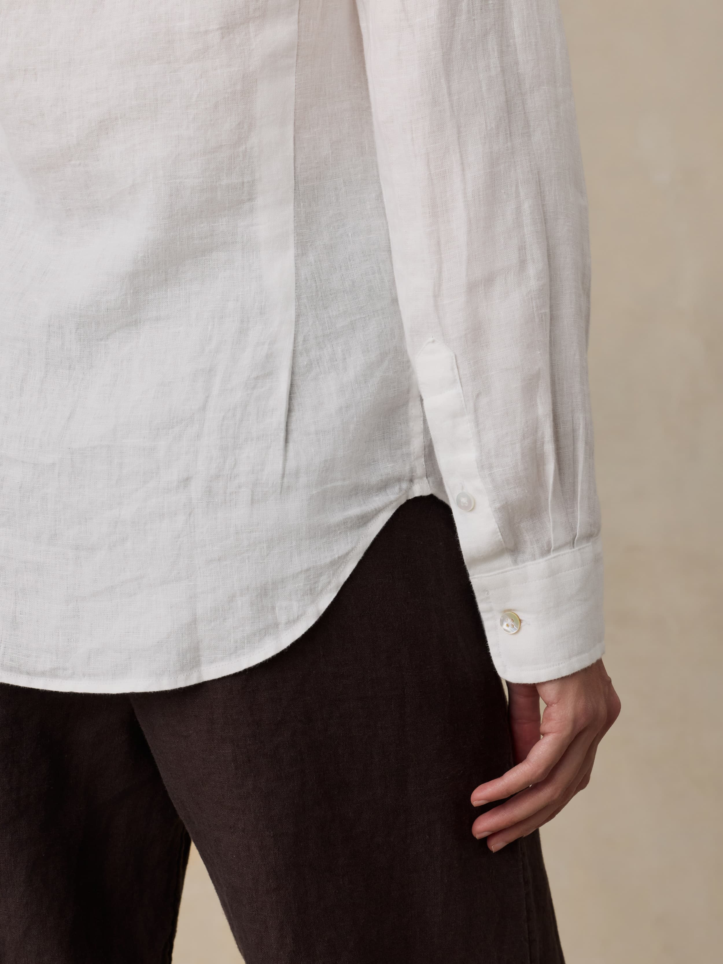 Woman wearing a white linen shirt and brown linen pants against a beige background