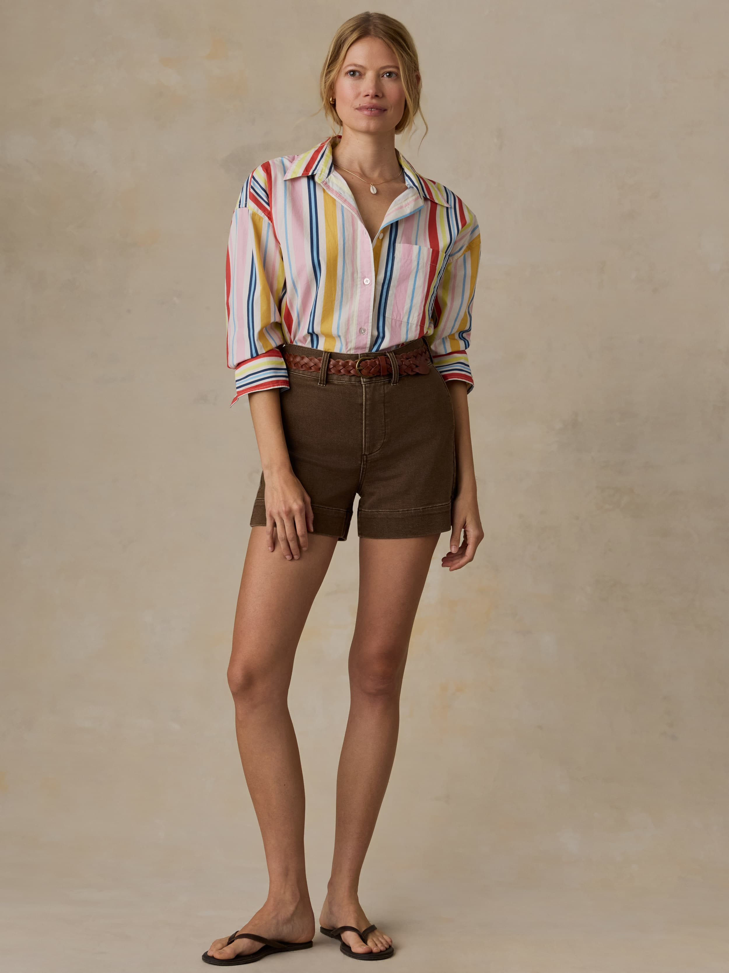 Woman wearing a colorful striped shirt and brown shorts against a beige background