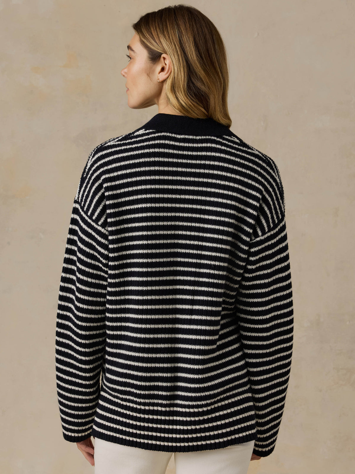 Woman wearing a blue and white striped sweater and white pants against a beige background, image 3 of 5