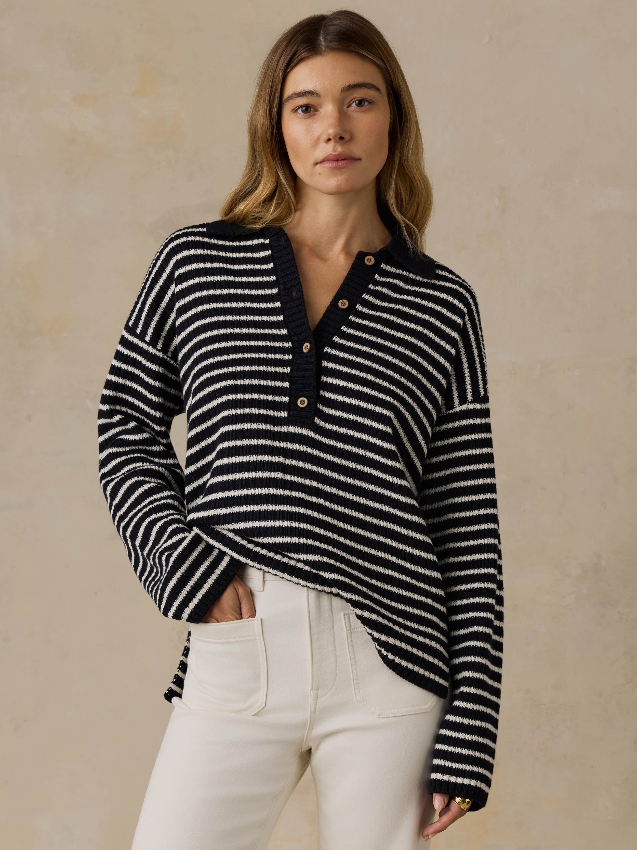 Woman wearing a blue and white striped sweater and white pants against a beige background