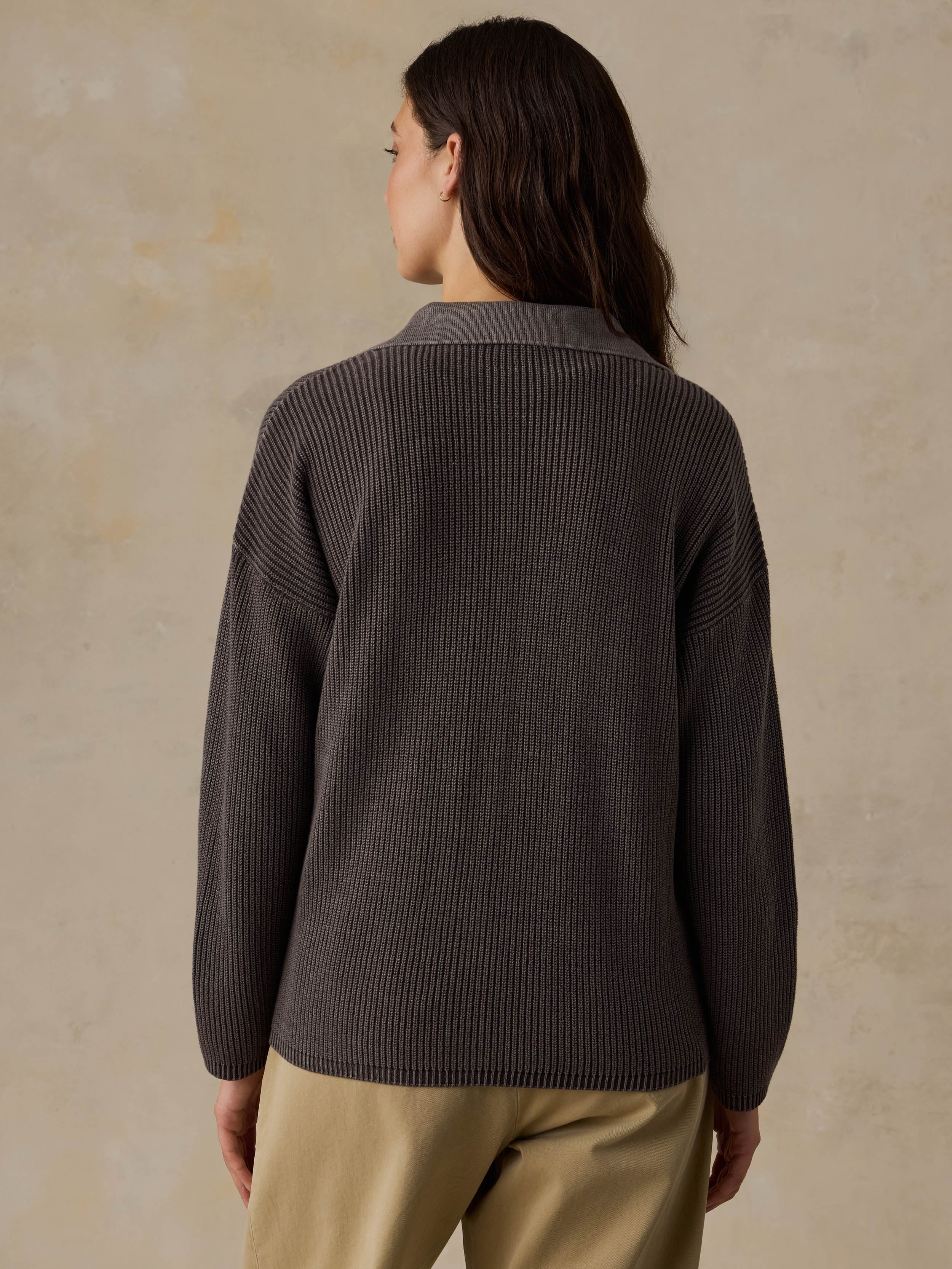 Woman wearing a brown sweater and beige pants against a beige background