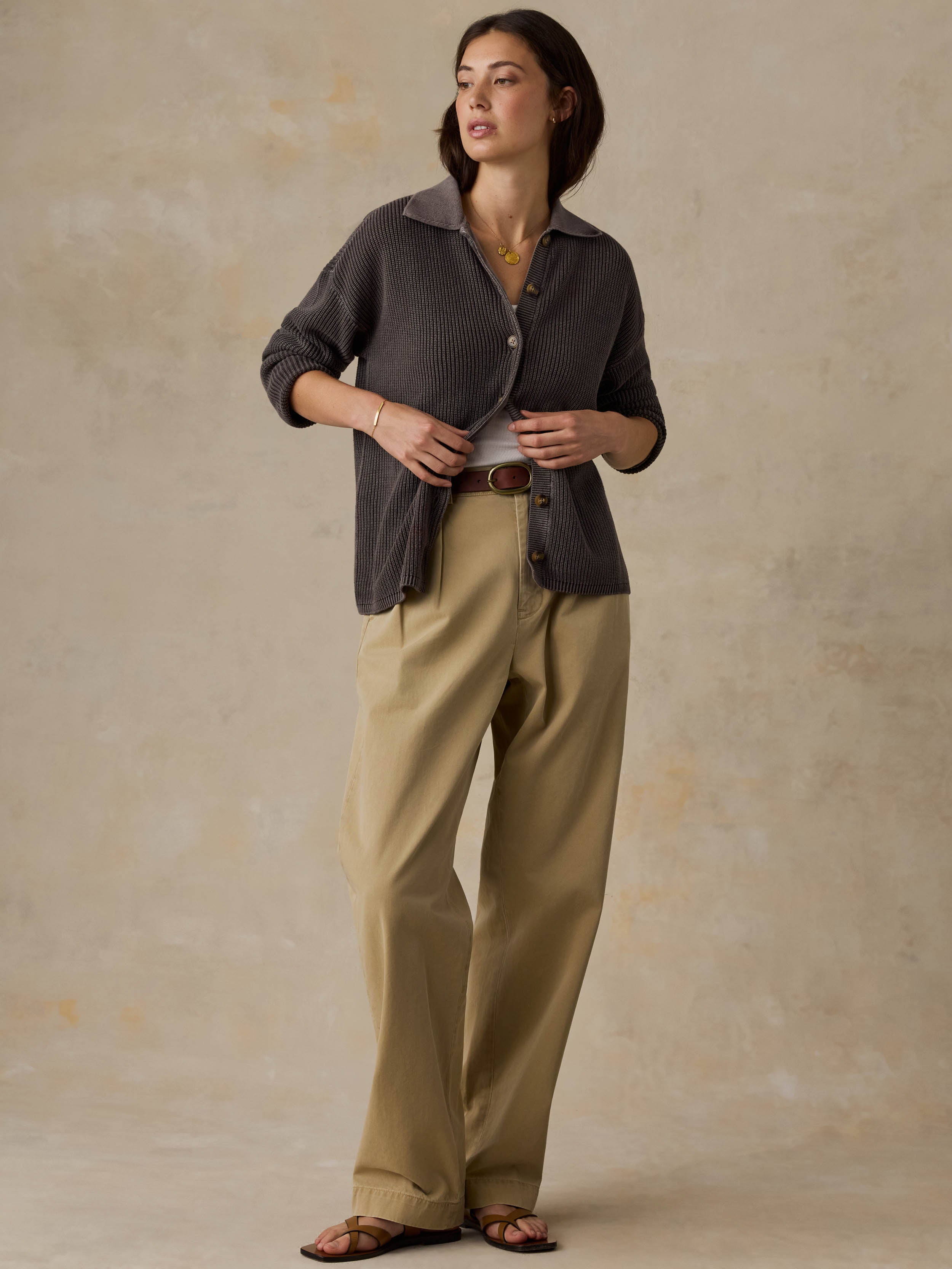 Woman wearing a brown sweater and beige pants against a beige background