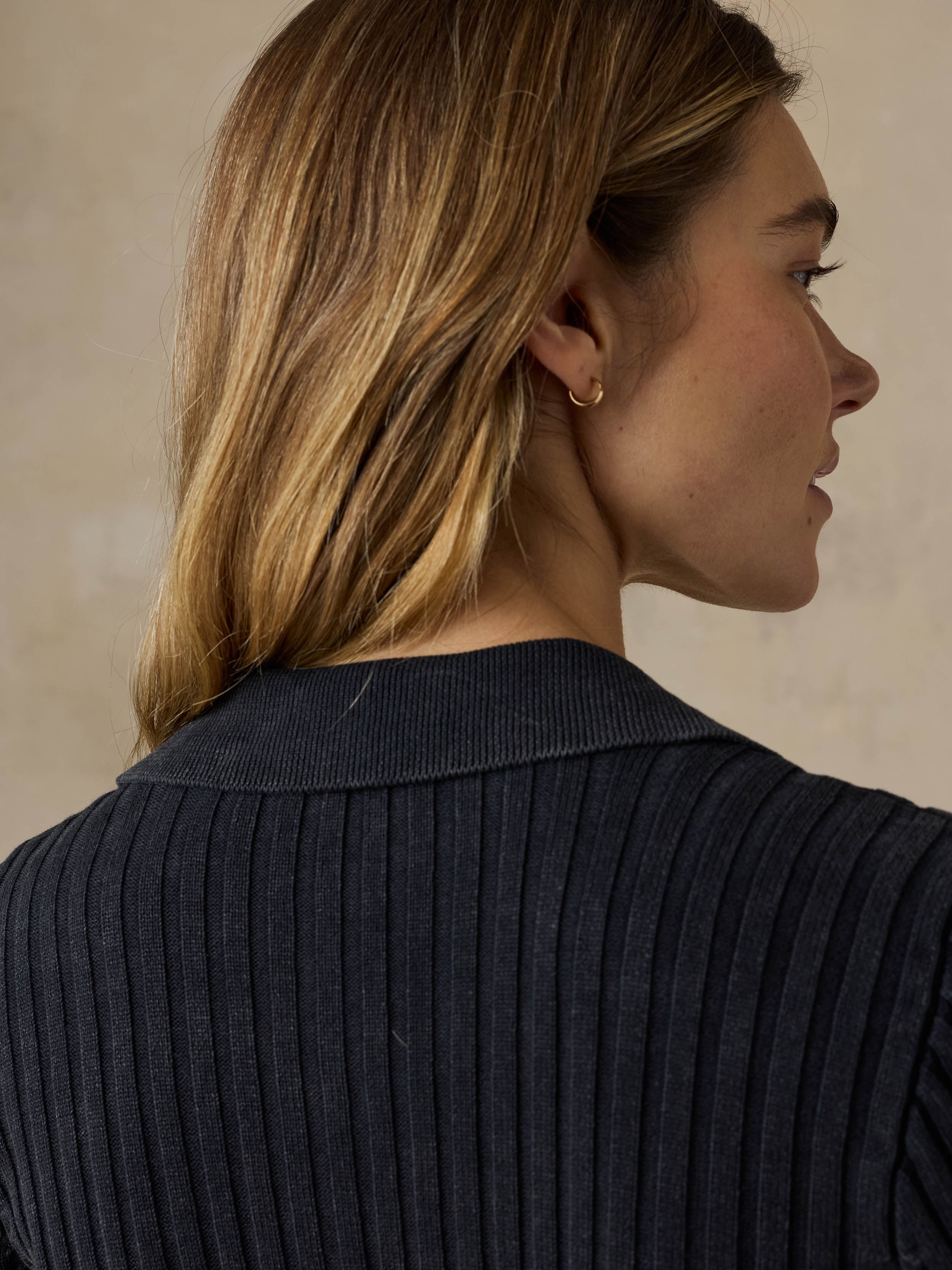 Woman wearing a black ribbed cardigan against a beige background