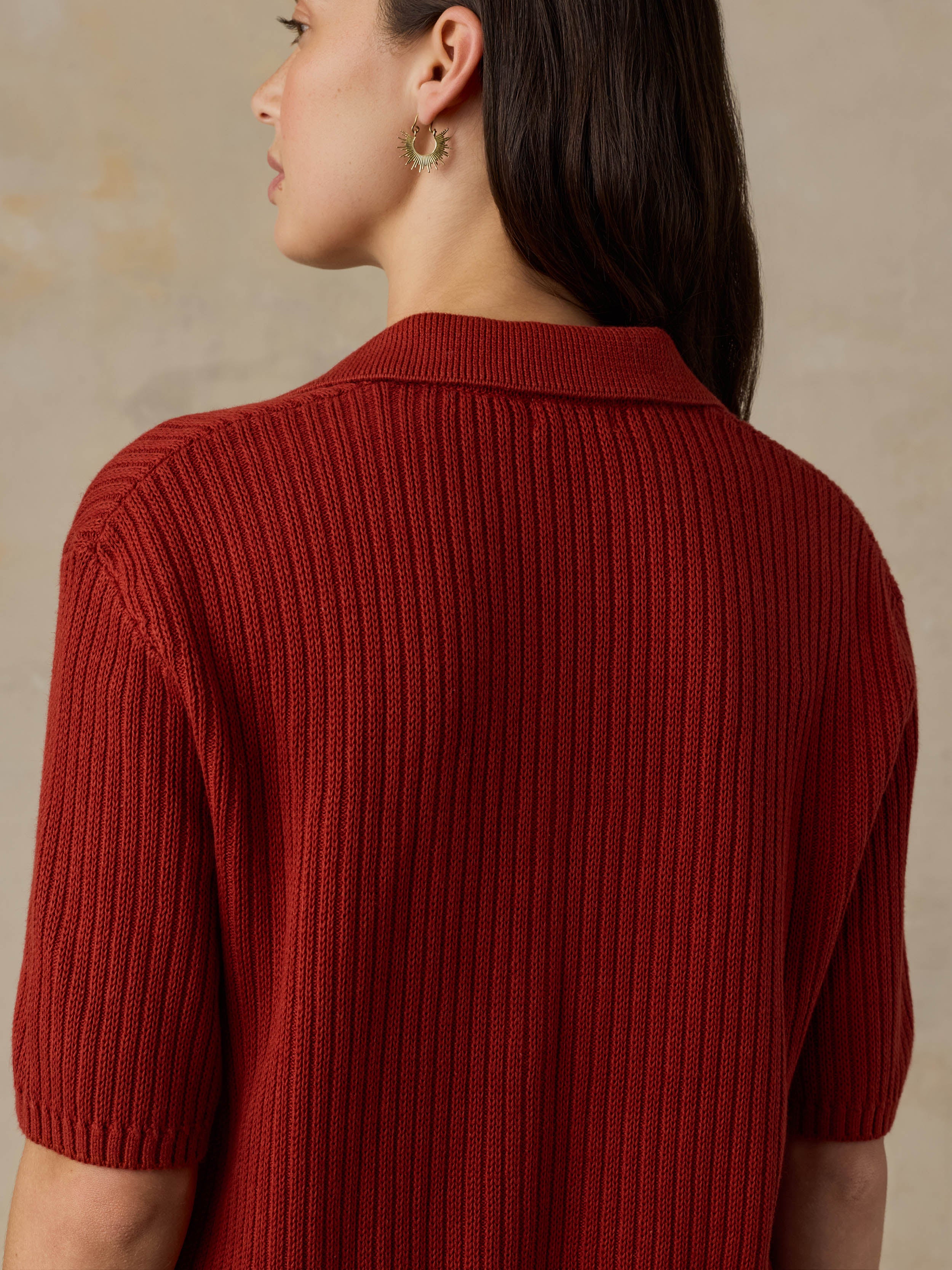 Woman wearing a red ribbed knit polo shirt against a beige background