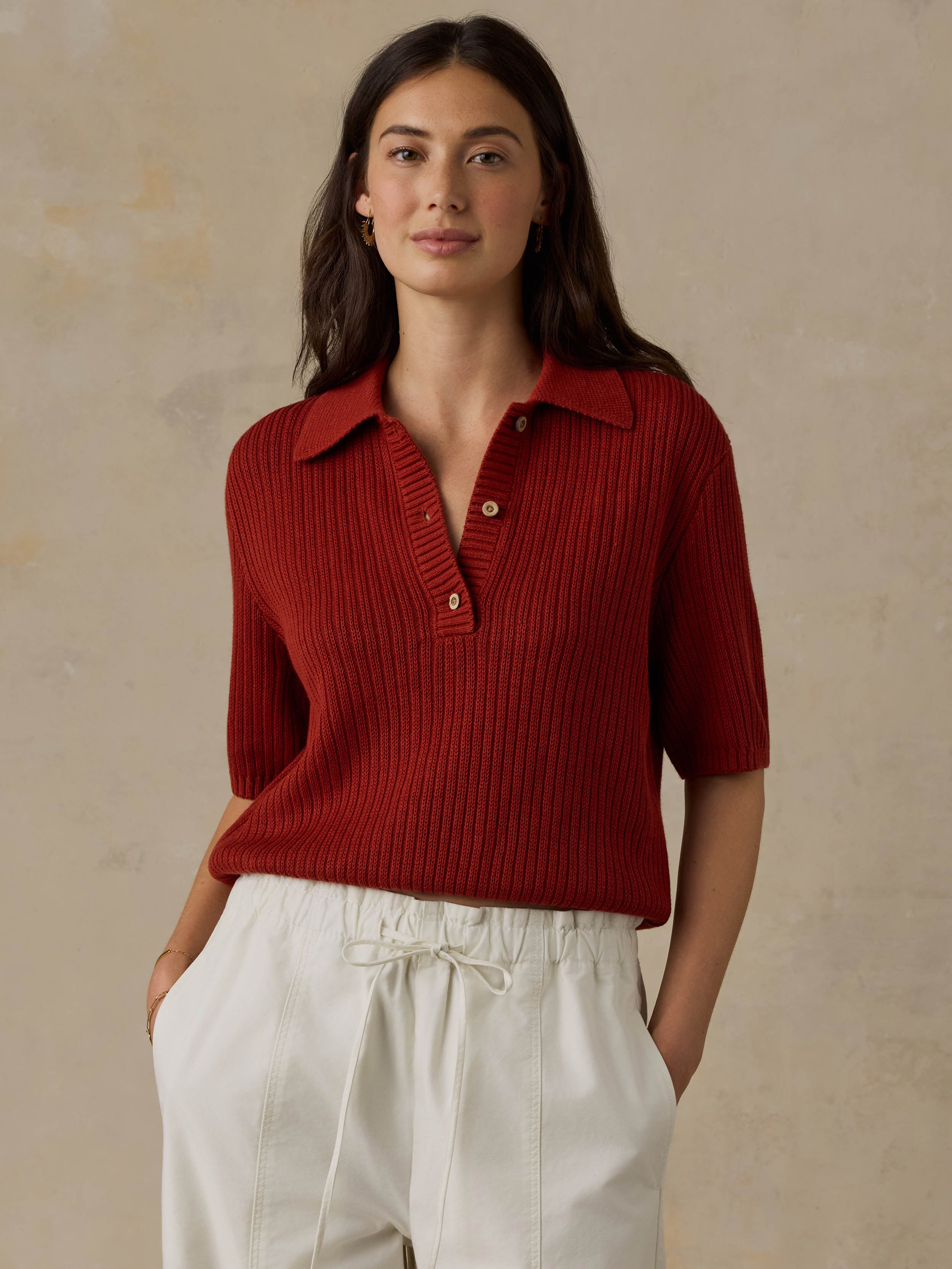 Woman wearing a red ribbed knit polo shirt and white pants against a beige background