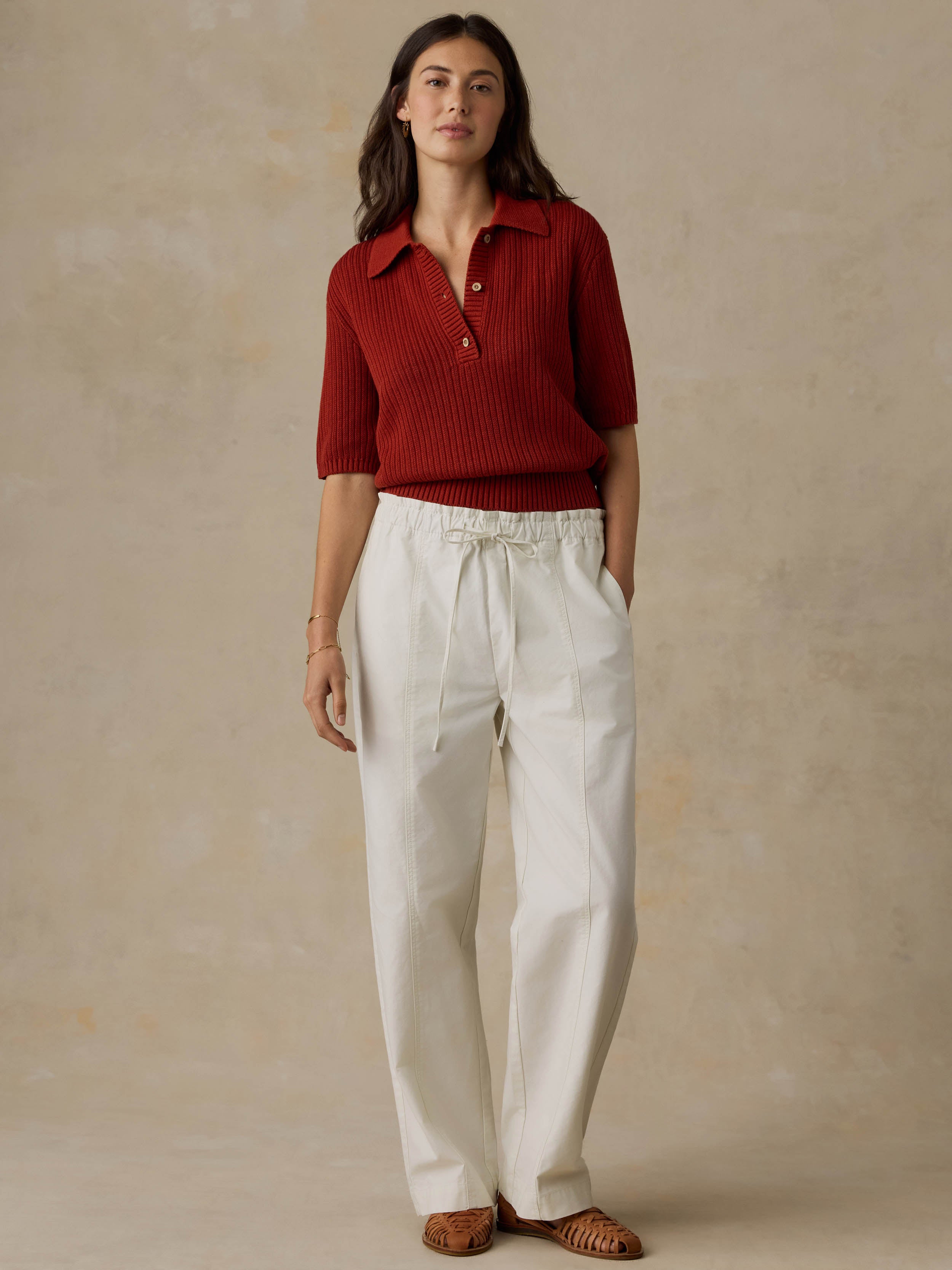 Woman wearing a red ribbed knit polo shirt and white pants against a beige background