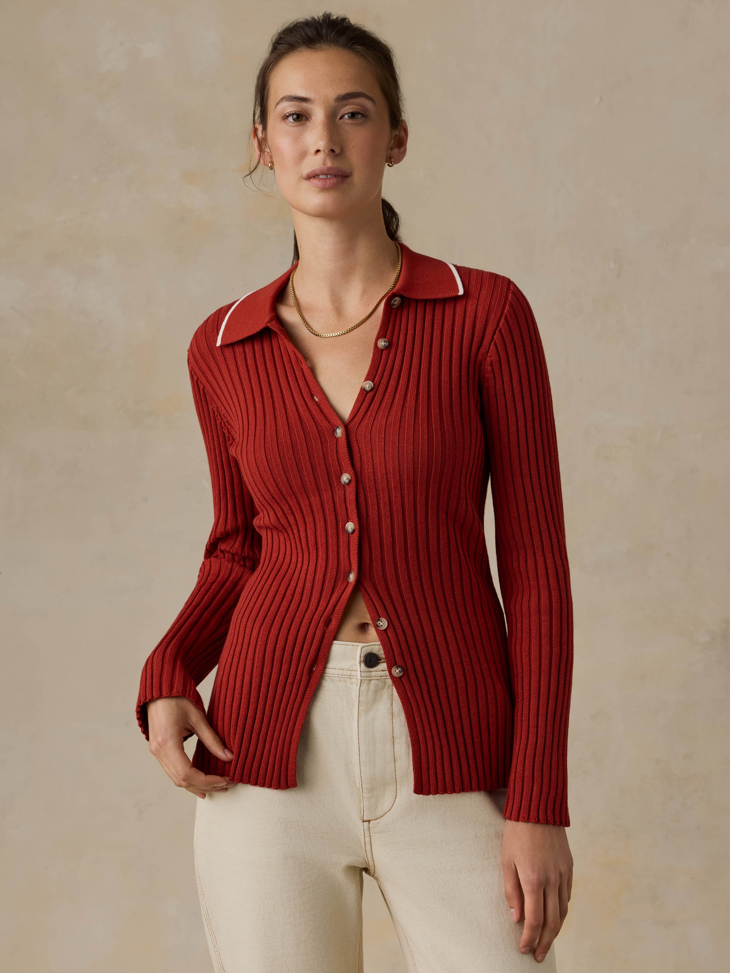 Woman wearing a red cardigan and white jeans against a beige background