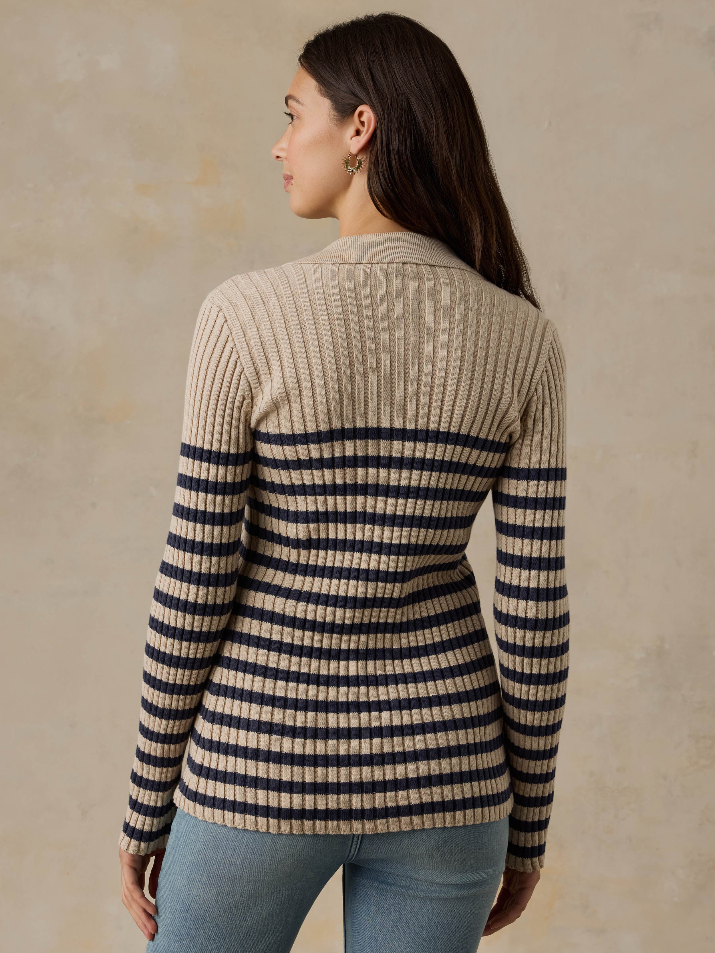 Woman wearing a beige and navy striped cardigan with blue jeans against a beige background