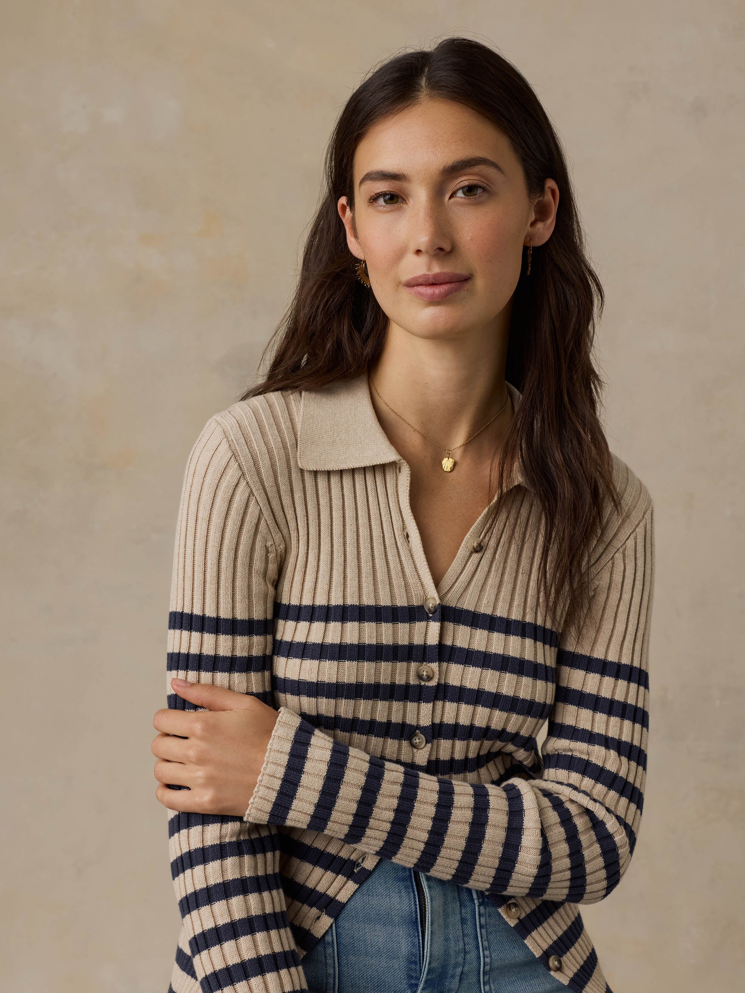 Woman wearing a beige and navy striped cardigan with blue jeans against a beige background
