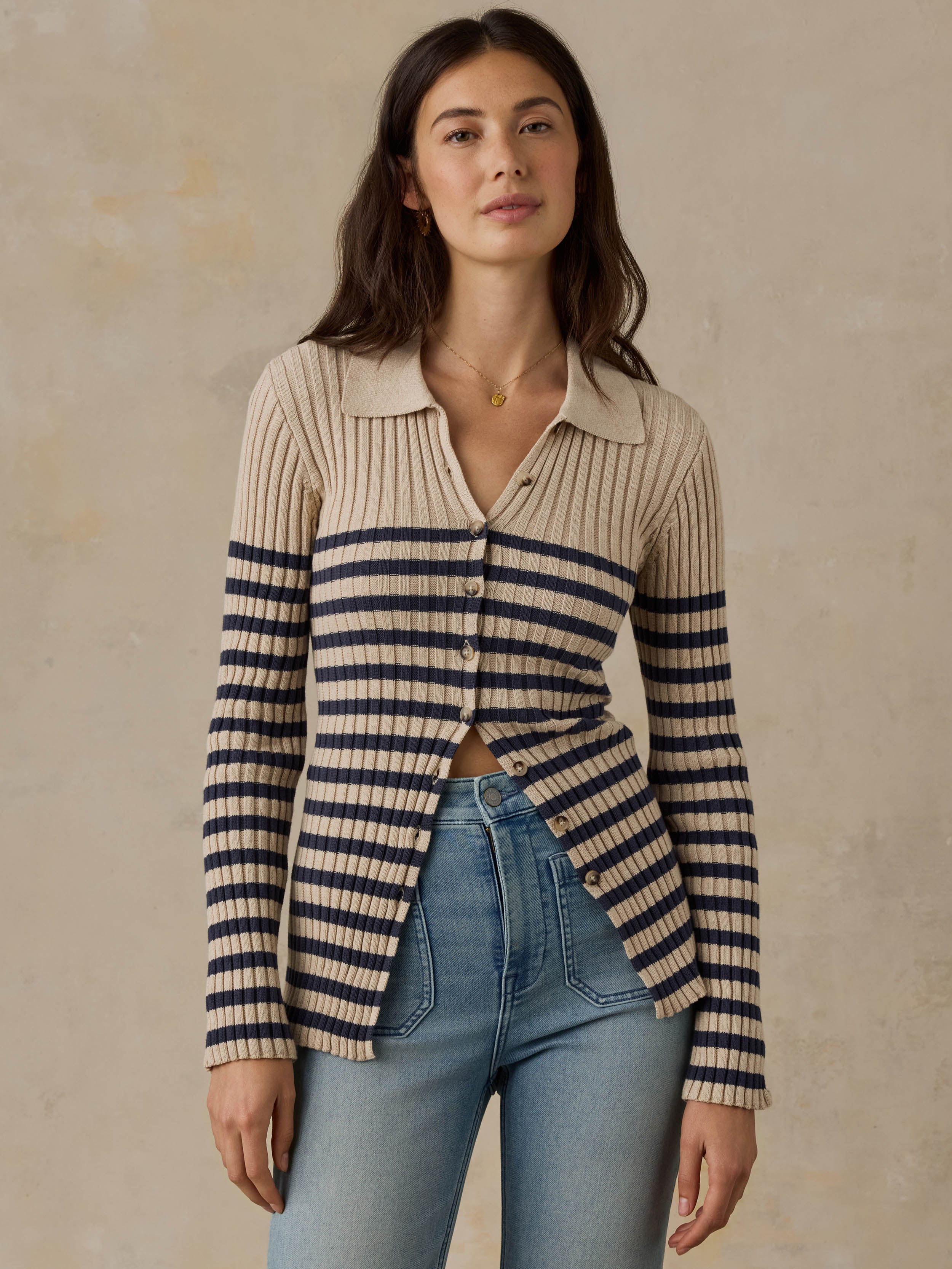 Woman wearing a beige and navy striped cardigan with blue jeans against a beige background
