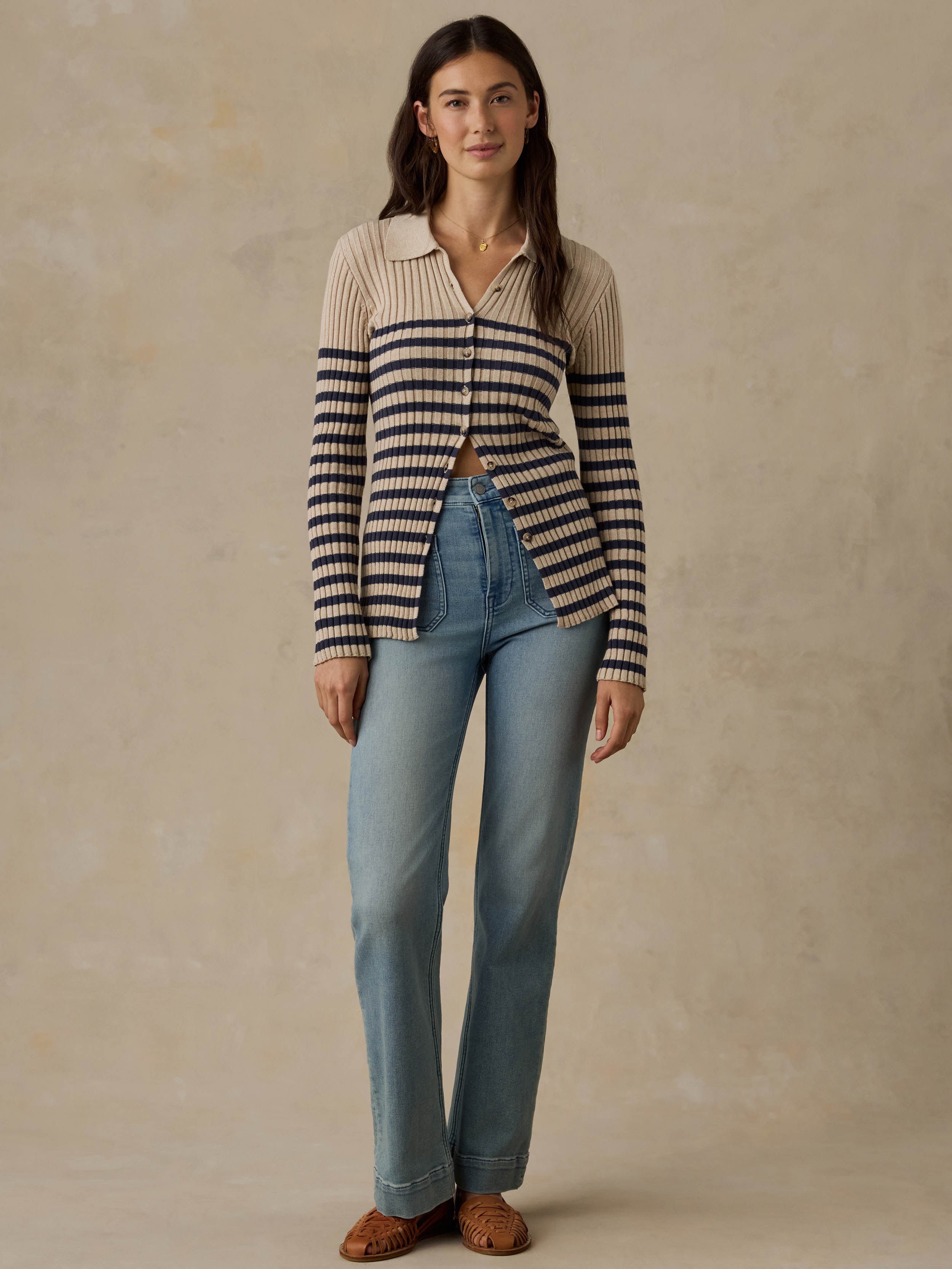 Woman wearing a beige and navy striped cardigan with blue jeans against a beige background
