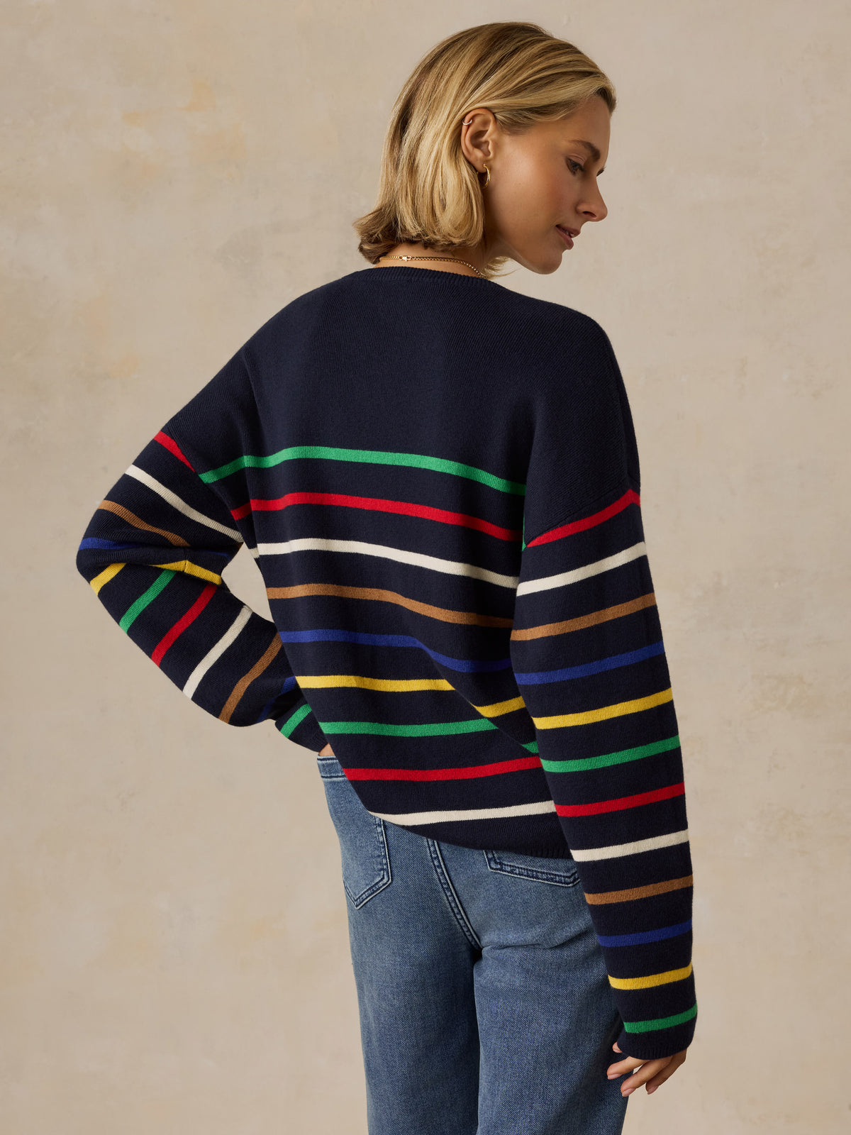 A woman viewed from behind wearing a colorful striped sweater and jeans, image 3 of 5