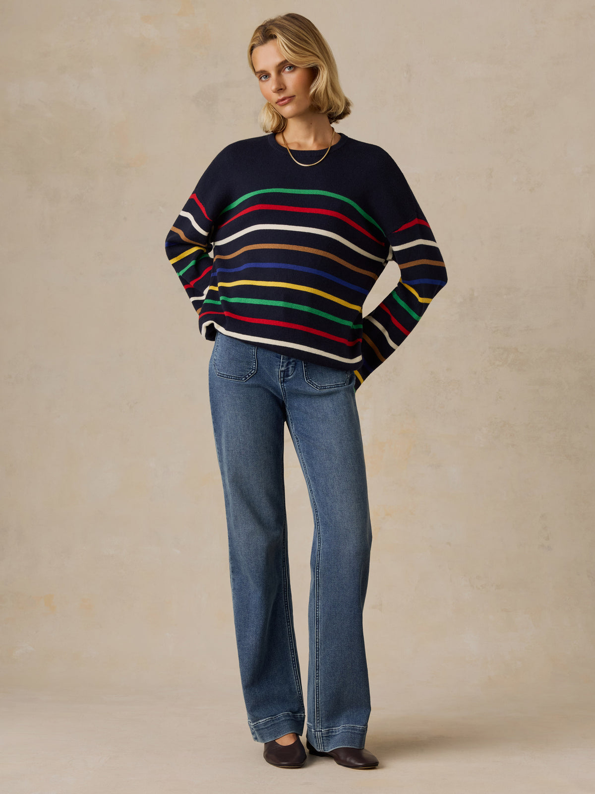 A woman wearing a colorful striped sweater and jeans, image 4 of 5