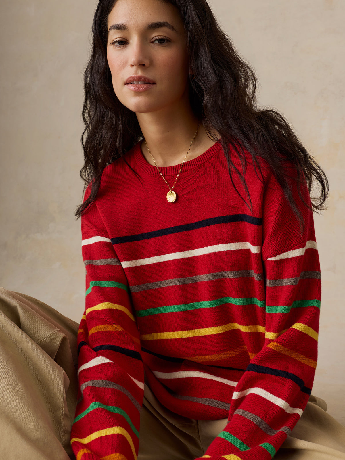 A woman wearing a red striped sweater and chino pants, image 4 of 5