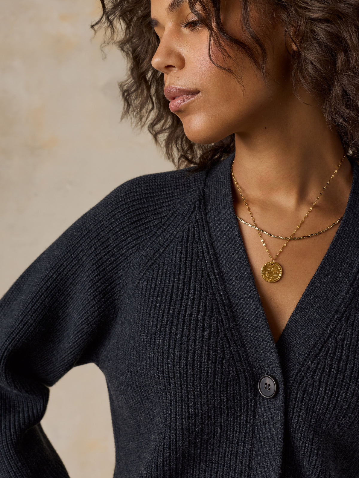 A close-up of a woman wearing a dark charcoal gray ribbed knit cardigan sweater, image 4 of 6