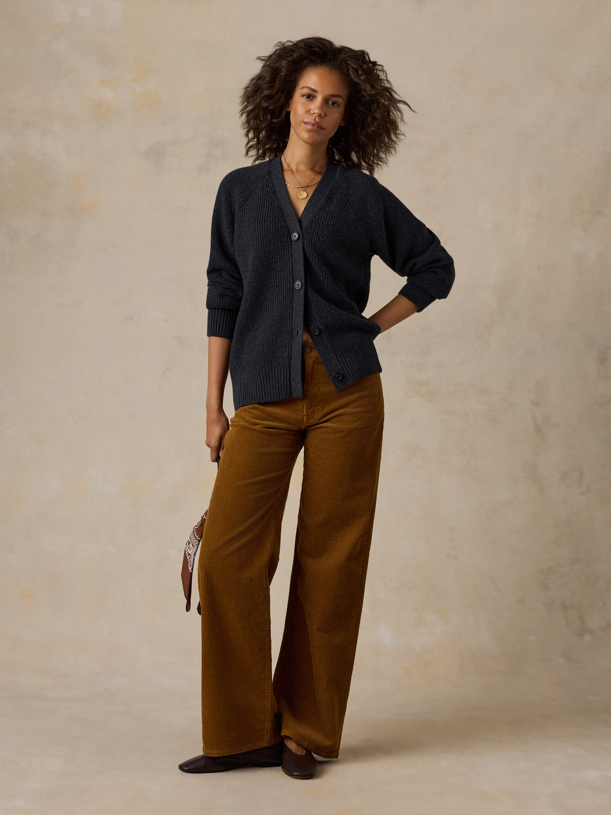 A woman wearing a dark navy cardigan, wide-leg brown pants, and dark flats, image 5 of 6