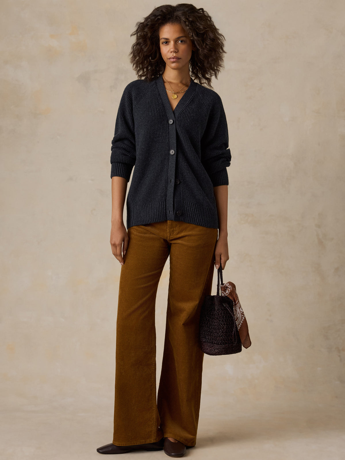 A model stands wearing a dark navy cardigan, wide-leg brown pants, and holding a dark woven handbag., image 6 of 6