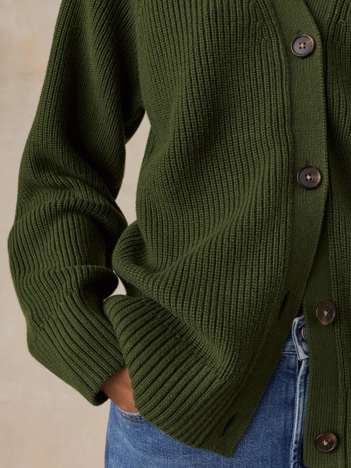 Close-up of a woman wearing an olive green ribbed knit cardigan with dark buttons, paired with blue jeans, image 4 of 6