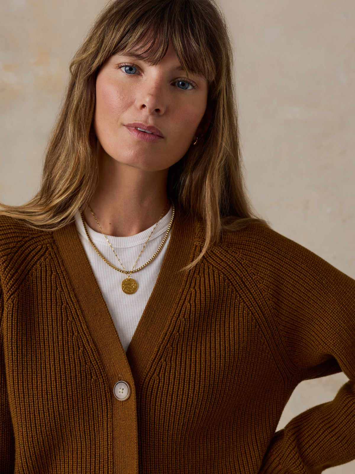 A woman wearing a ribbed brown cardigan over a white top, styled with layered gold necklaces, image 2 of 5